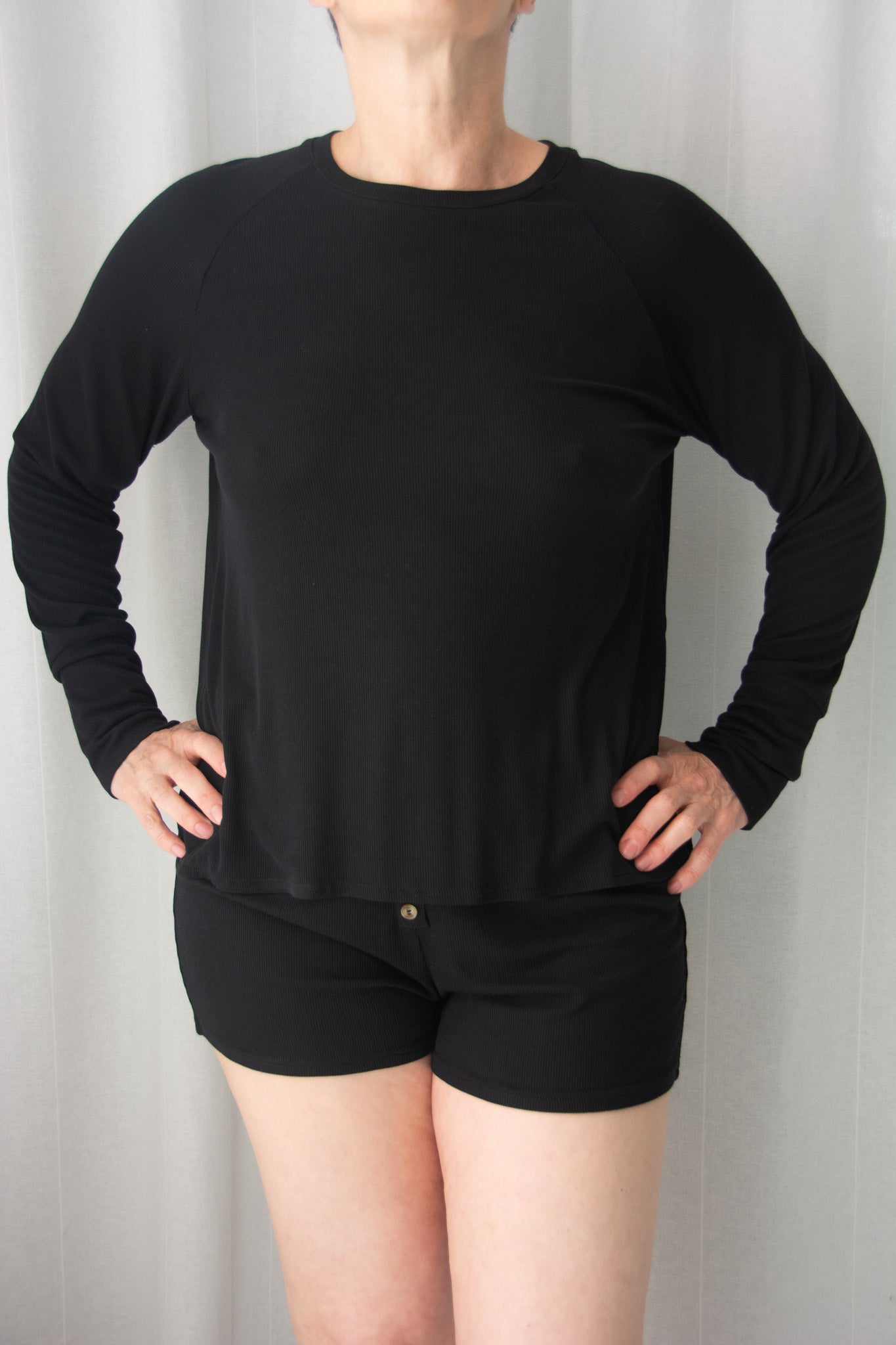 Person wearing a black long-sleeve top and black shorts against a plain background