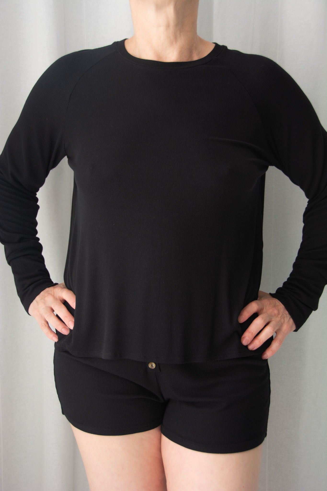 Person wearing a black long-sleeve top and black shorts against a plain background