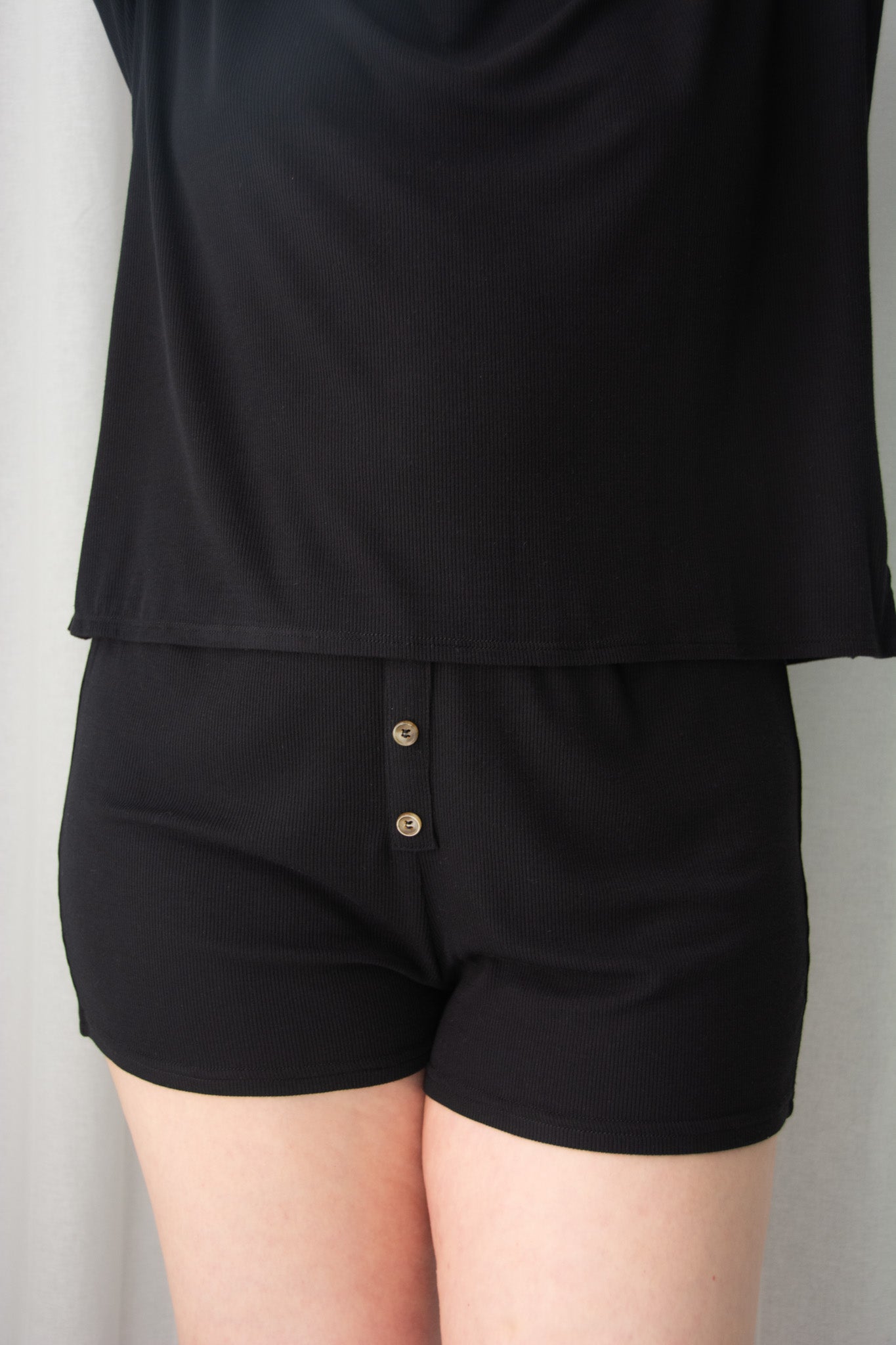 Person wearing a black top and shorts set on a plain background