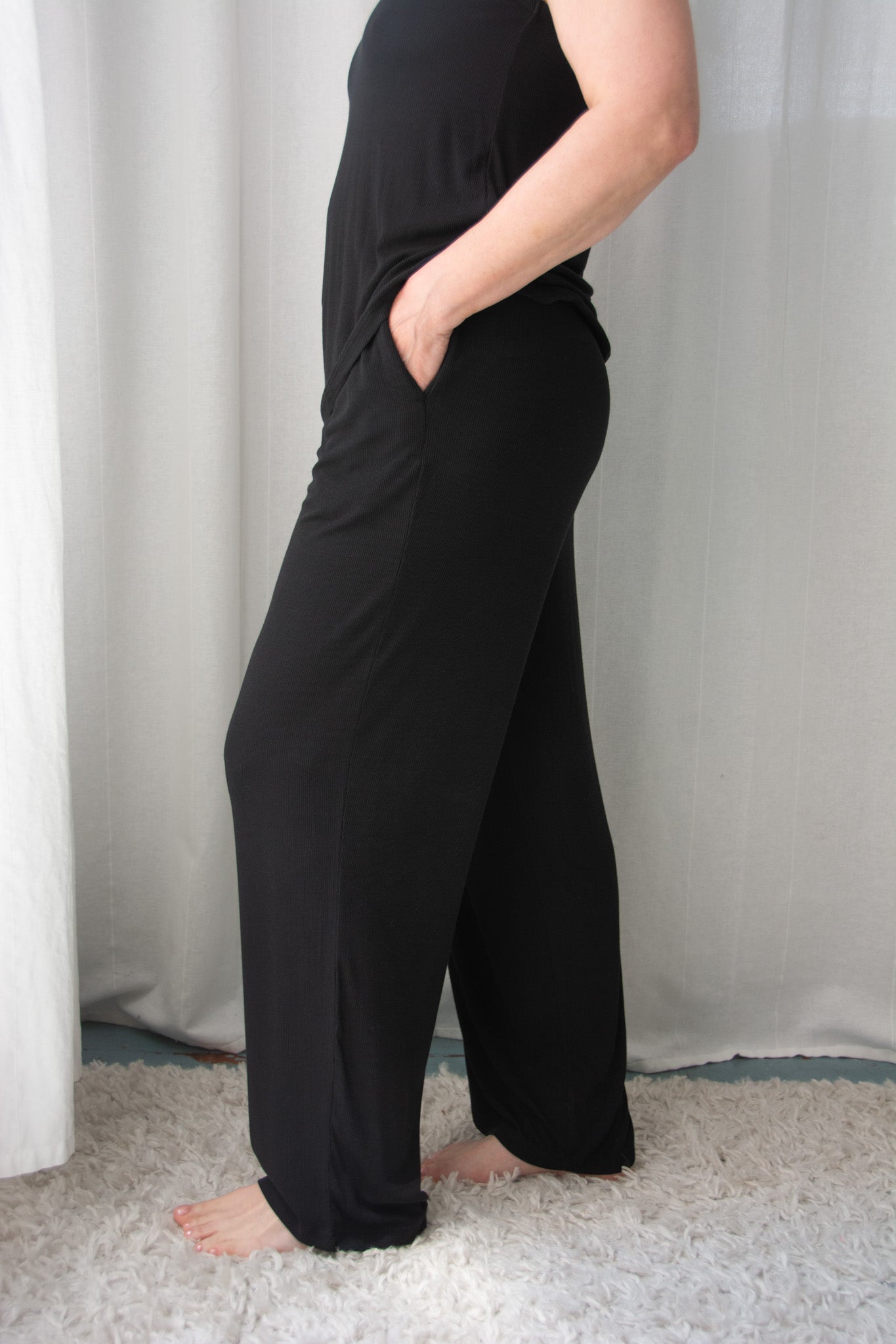 Person wearing black wide-leg pants standing against a white curtain.