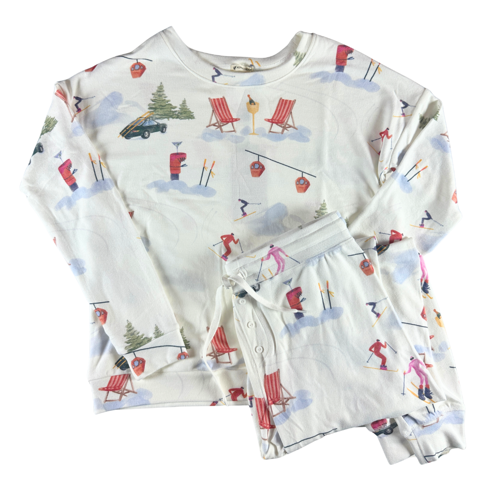 white long pajamas with illustrations of skiers, trees, and other various winter scenes. against a white background.