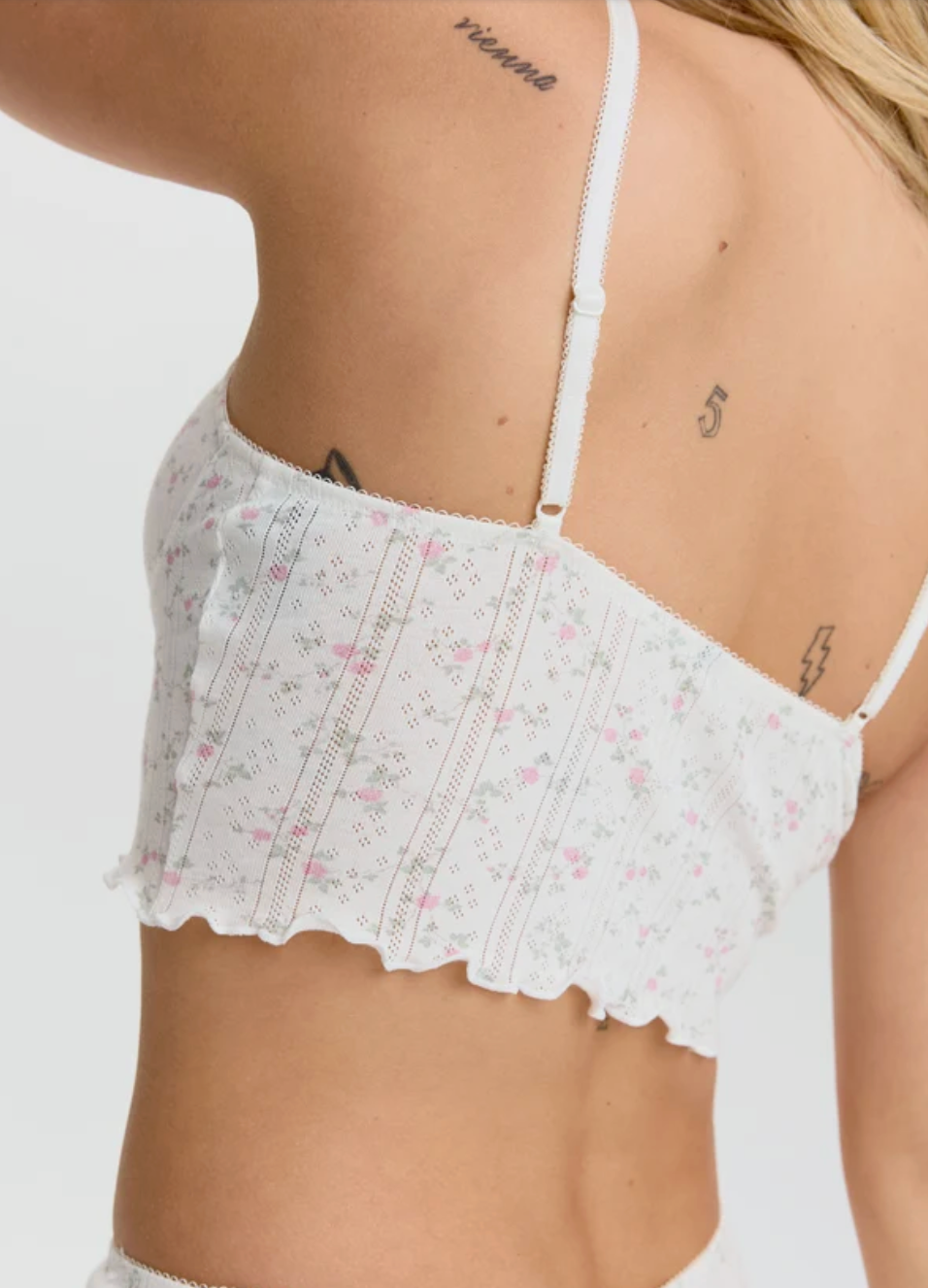 Close-up back view of a woman wearing a white lace crop top with a delicate pink and green floral print, showing the thin straps and lace back detail.