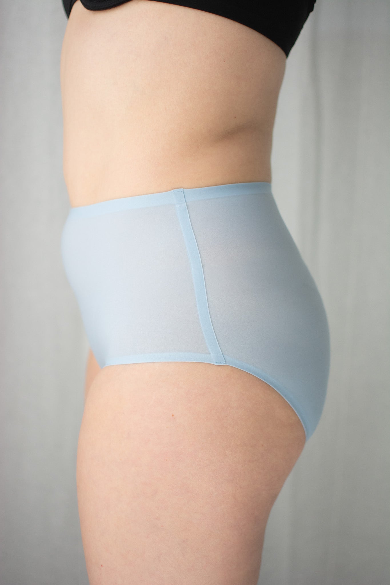 Person wearing blue underwear and black bra against a neutral background.