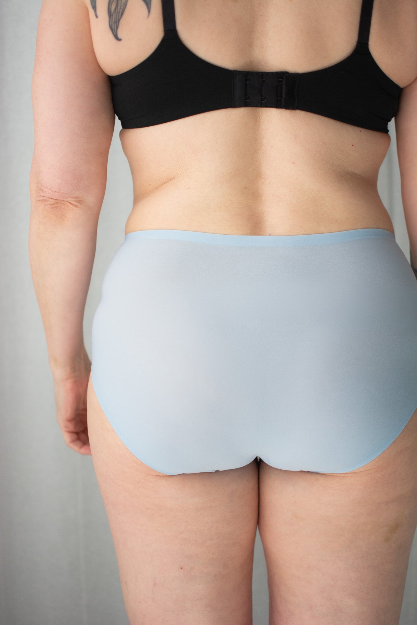 Person wearing a black bra and light blue underwear on a plain background