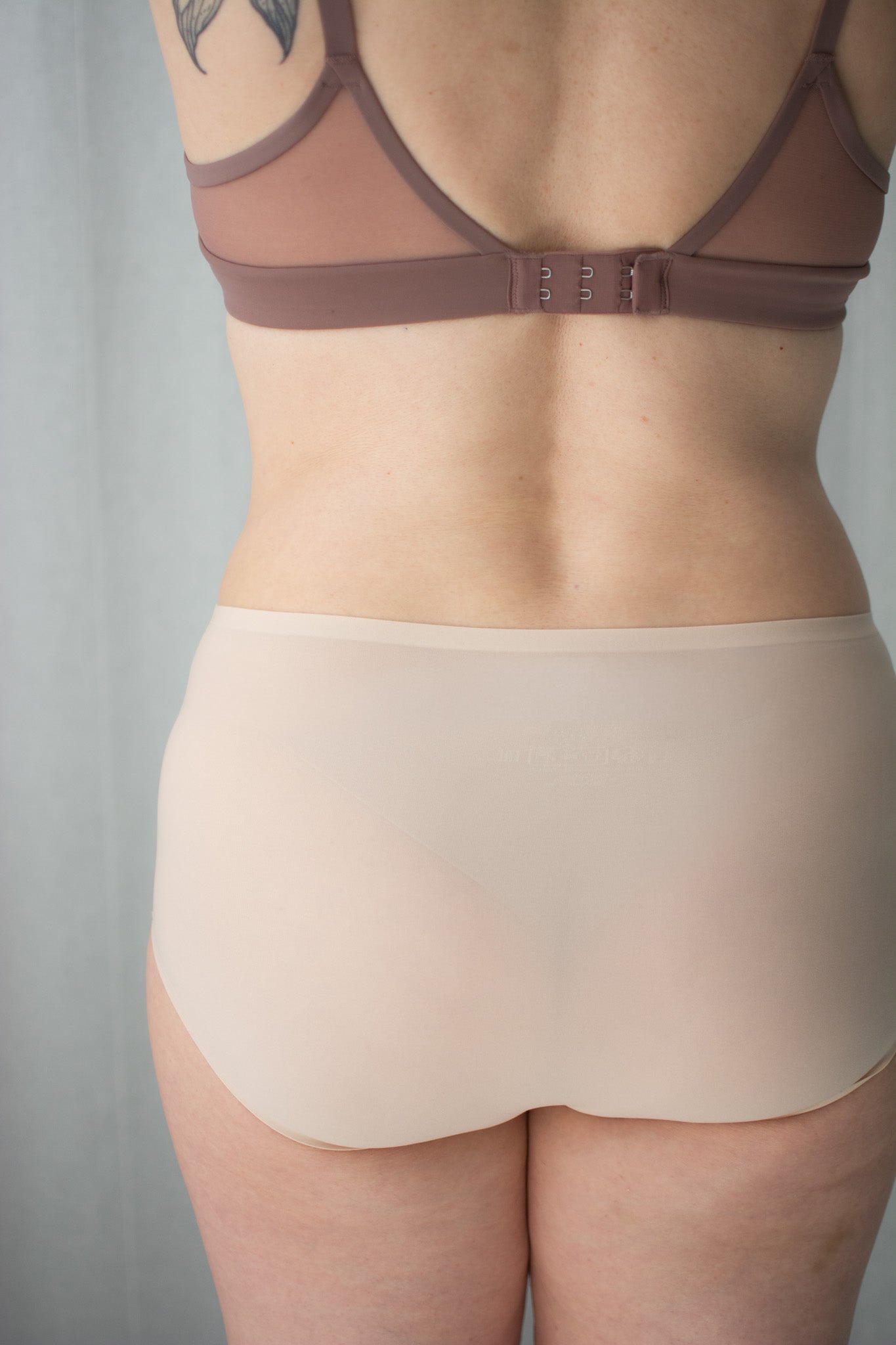 Person wearing neutral bra and underwear against a white background.