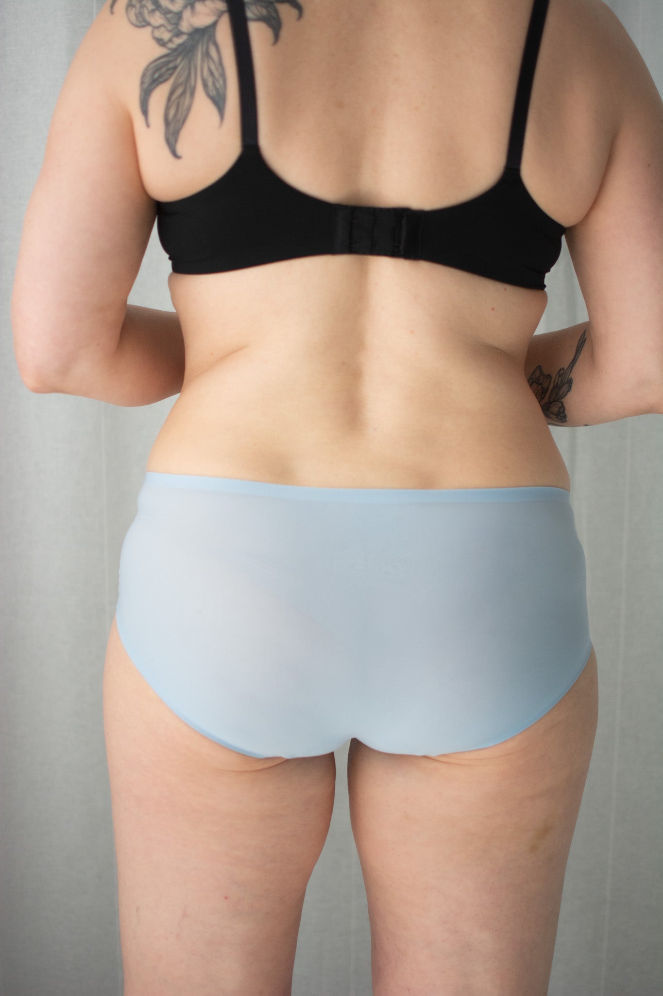 Person wearing a black bra and light blue underwear against a neutral background