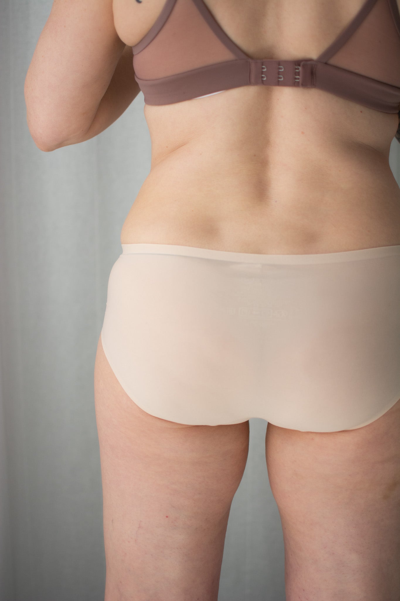 Person wearing a brown bra and beige underwear against a gray background