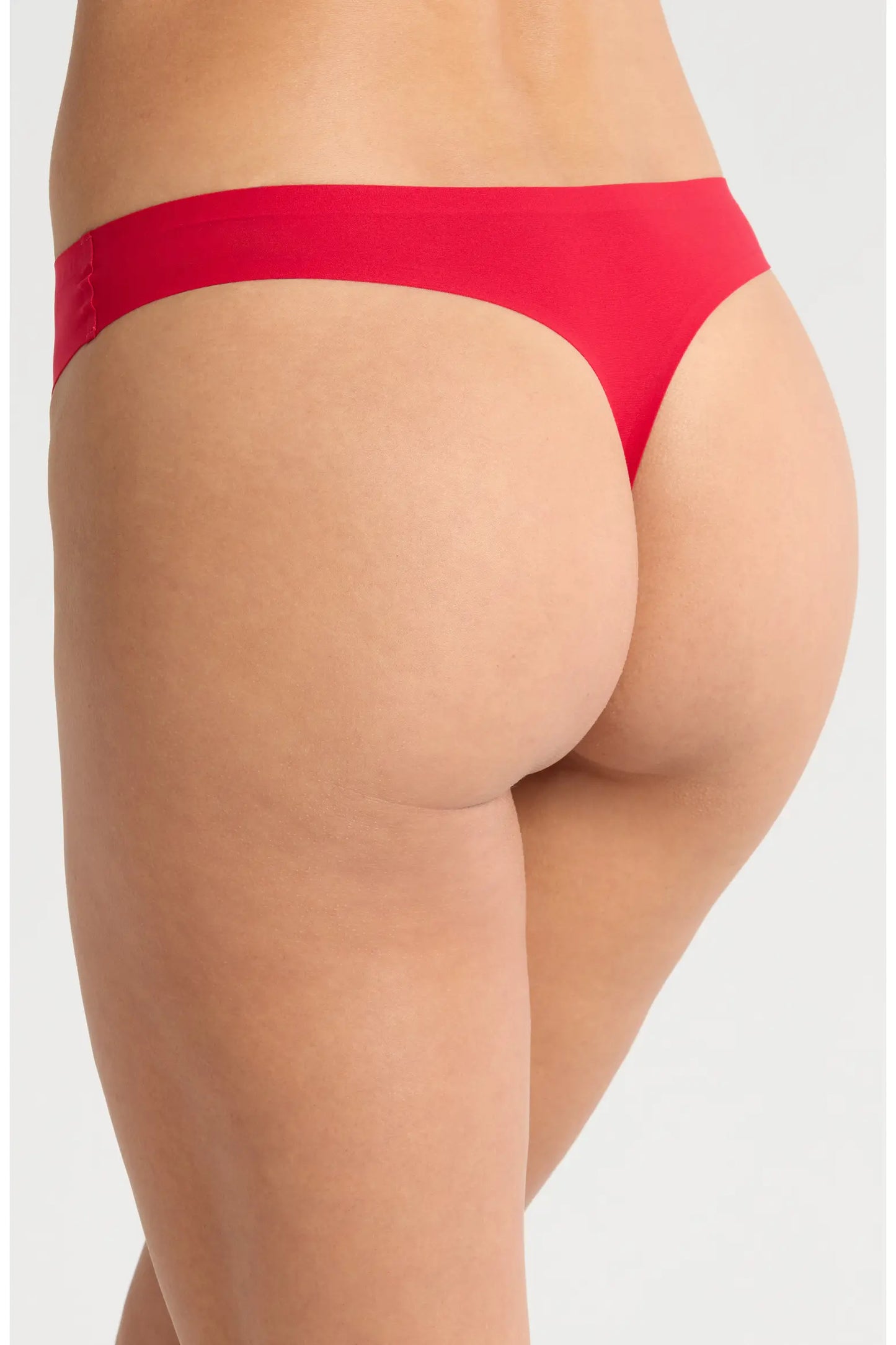 Rear view of a model wearing a bright red thong-style underwear bottom against a light gray studio background.