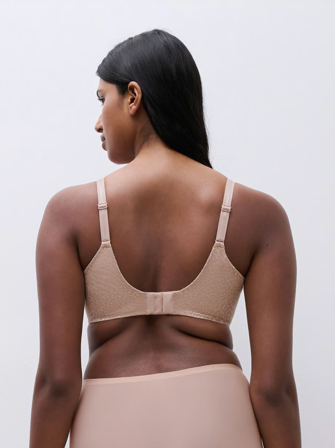 Woman wearing a beige bra and underwear set against a plain background