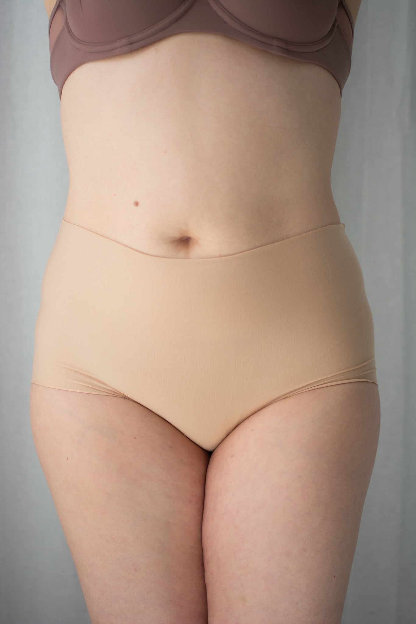 Beige shapewear being worn against a gray background