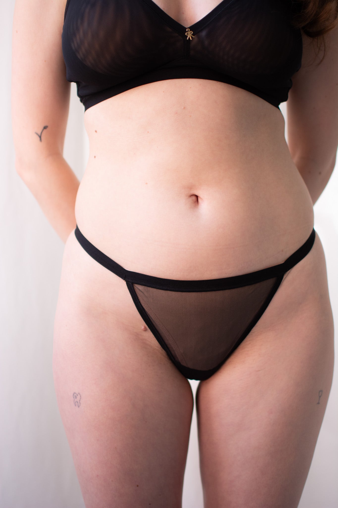 Person wearing a black mesh lingerie set against a plain background