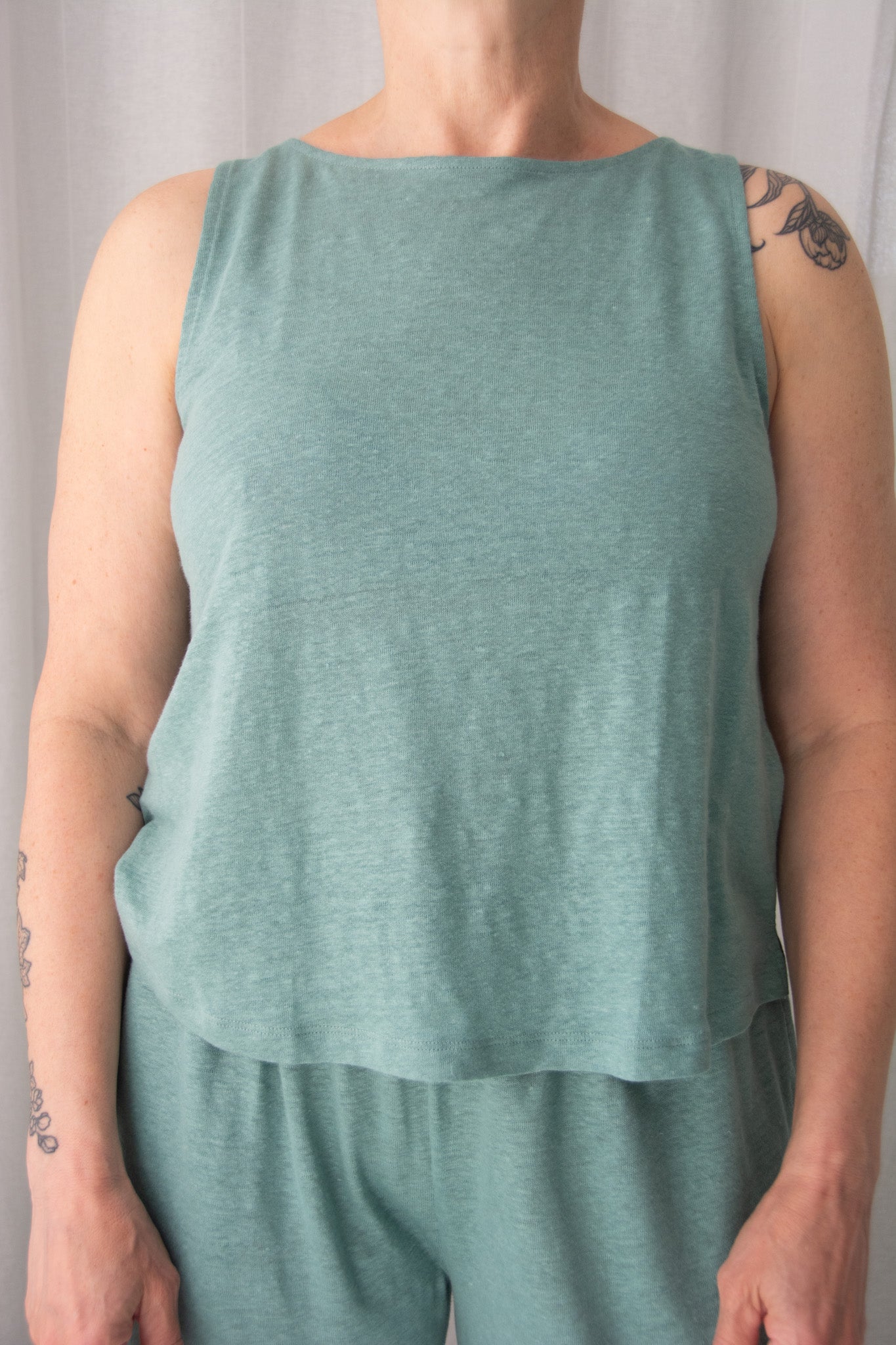 Person wearing a green sleeveless top and pants against a neutral background