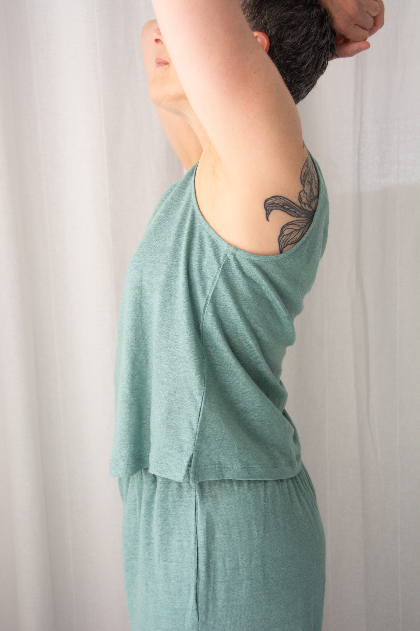 Person wearing a teal outfit with a tattoo on their arm against a white curtain background