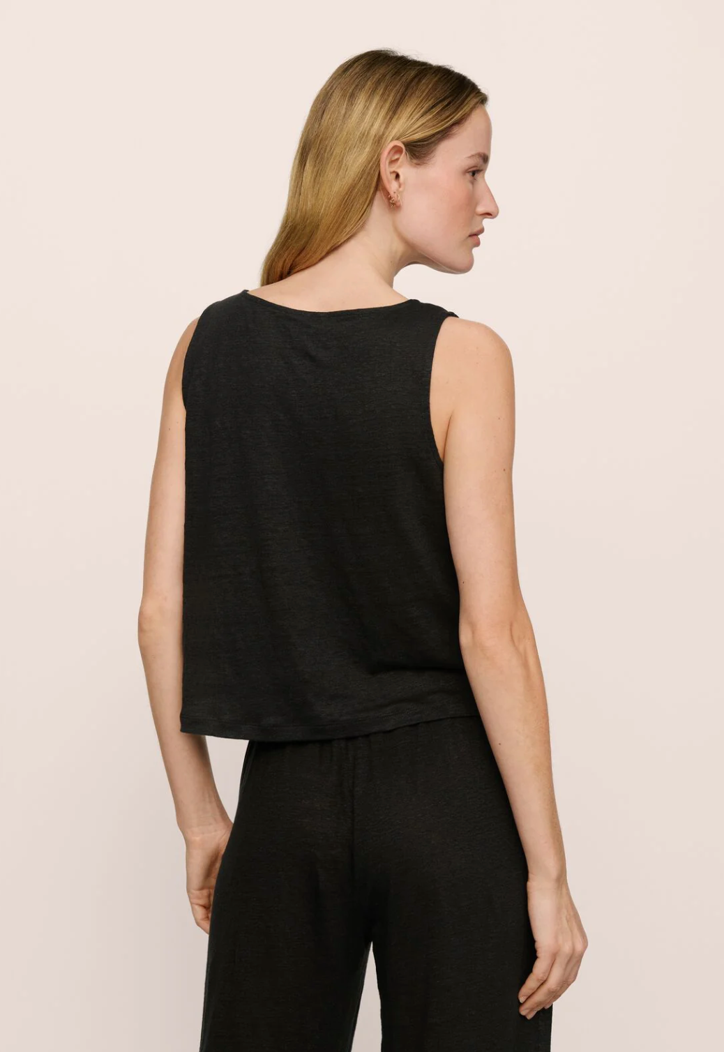 Woman wearing a black sleeveless top and pants on a light pink background