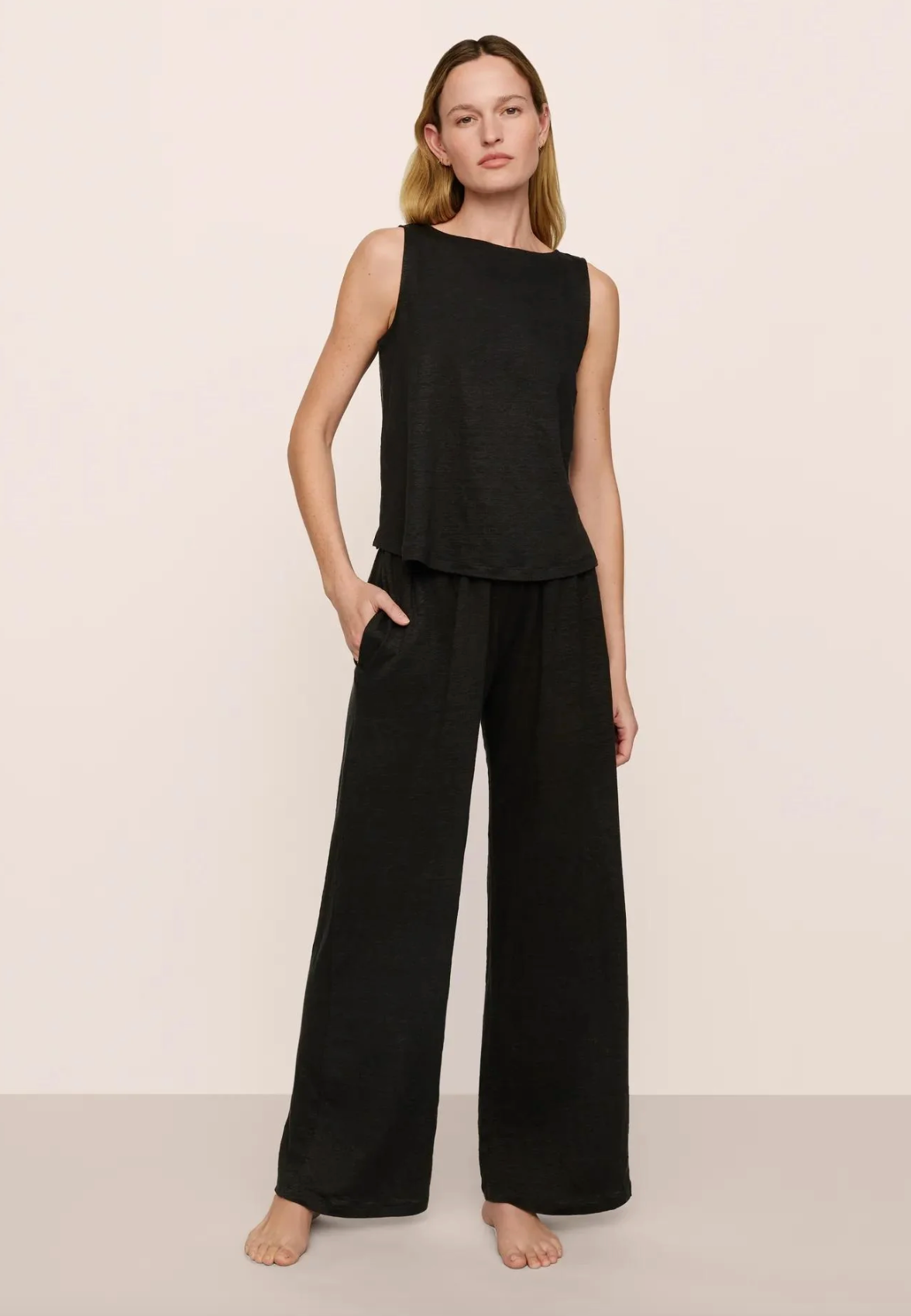 Woman wearing a black sleeveless top and wide-leg pants on a beige background