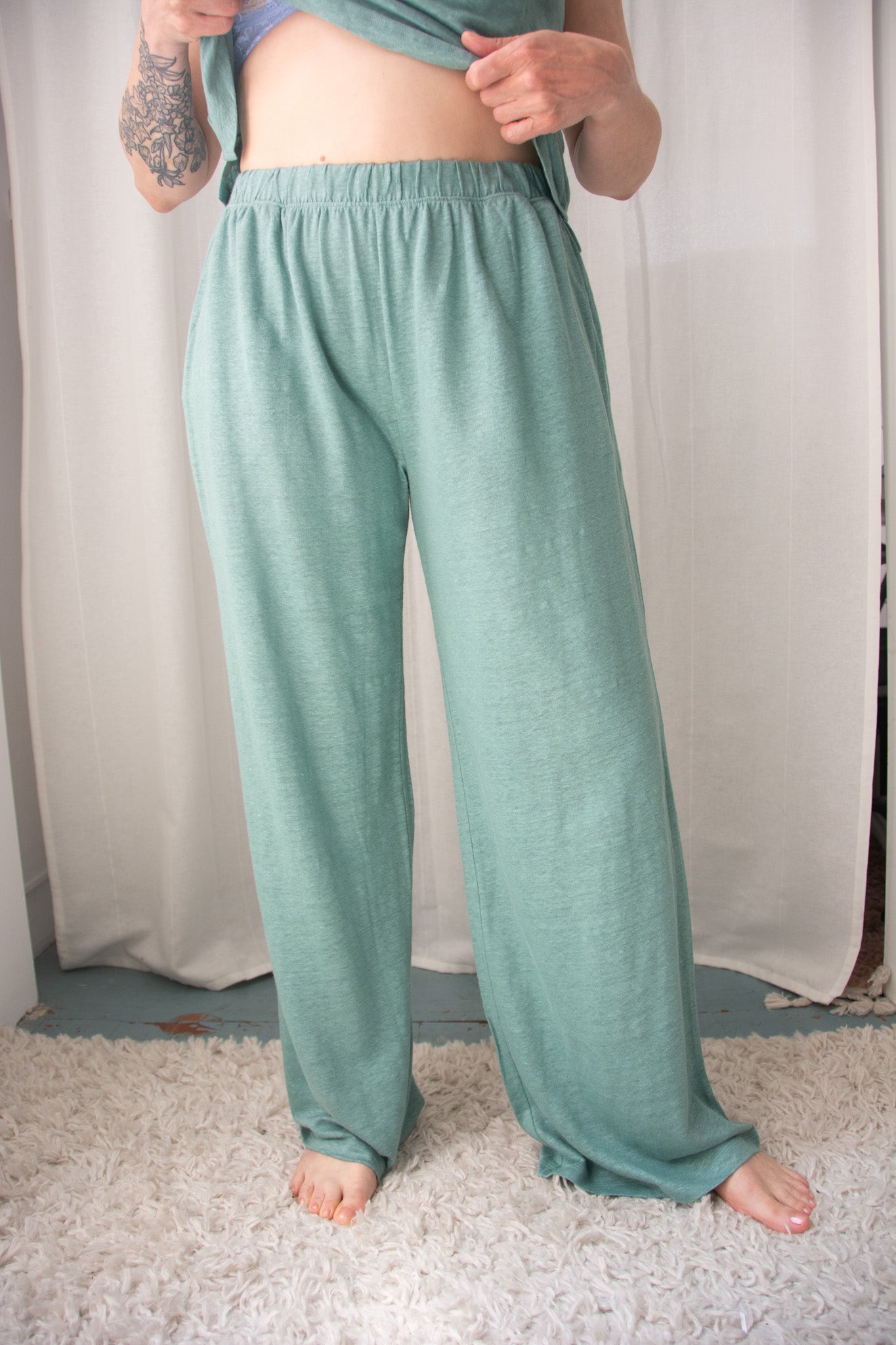 Person wearing teal pajama pants standing against a white curtain background