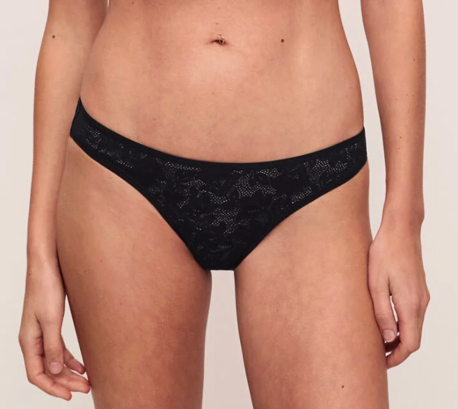 Black lace bikini briefs worn by a model, shown from the waist to upper thighs against a plain light beige studio background.