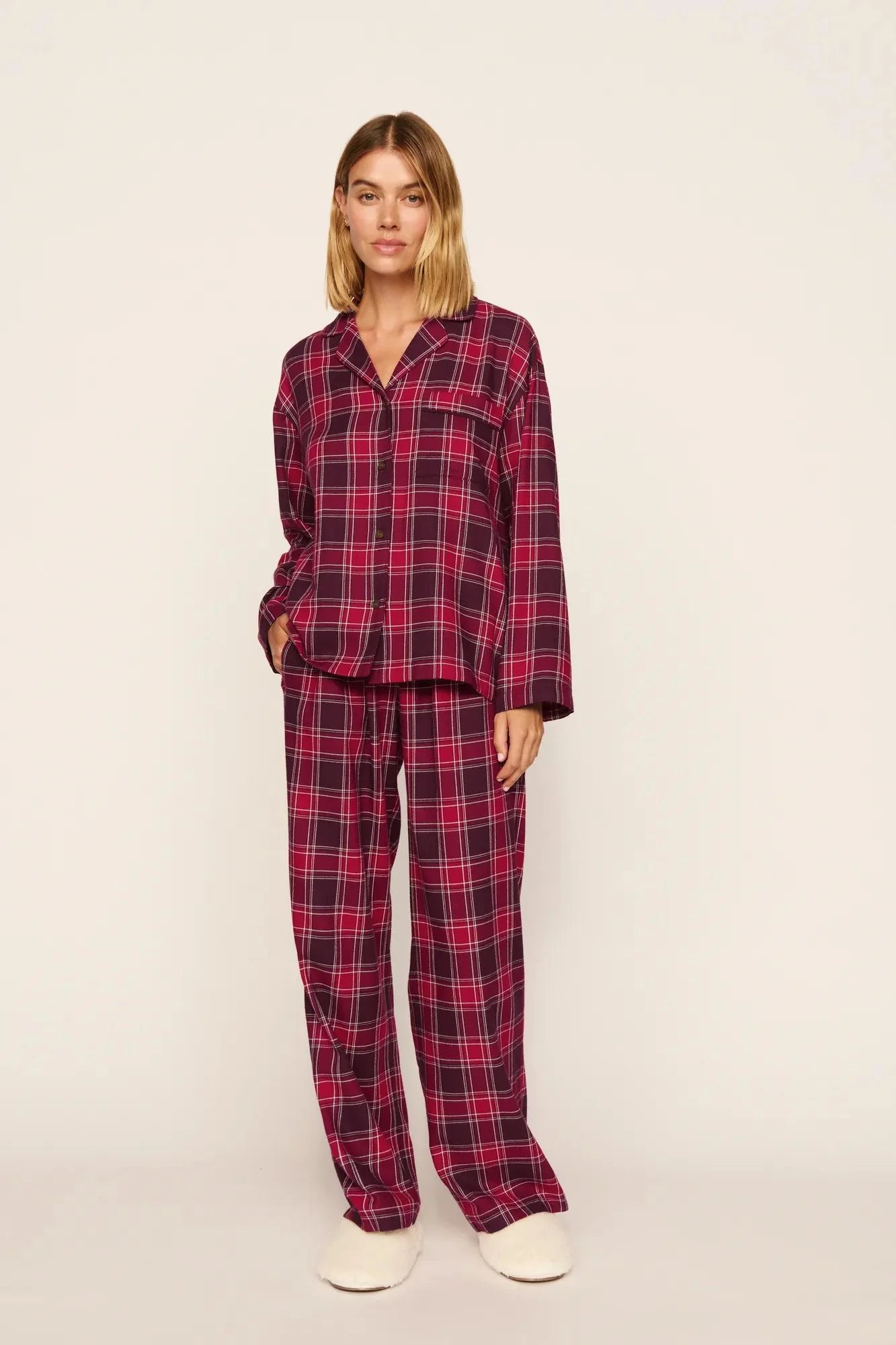 Model in a plaid, berry red long sleeve pajama set on a plain background. 