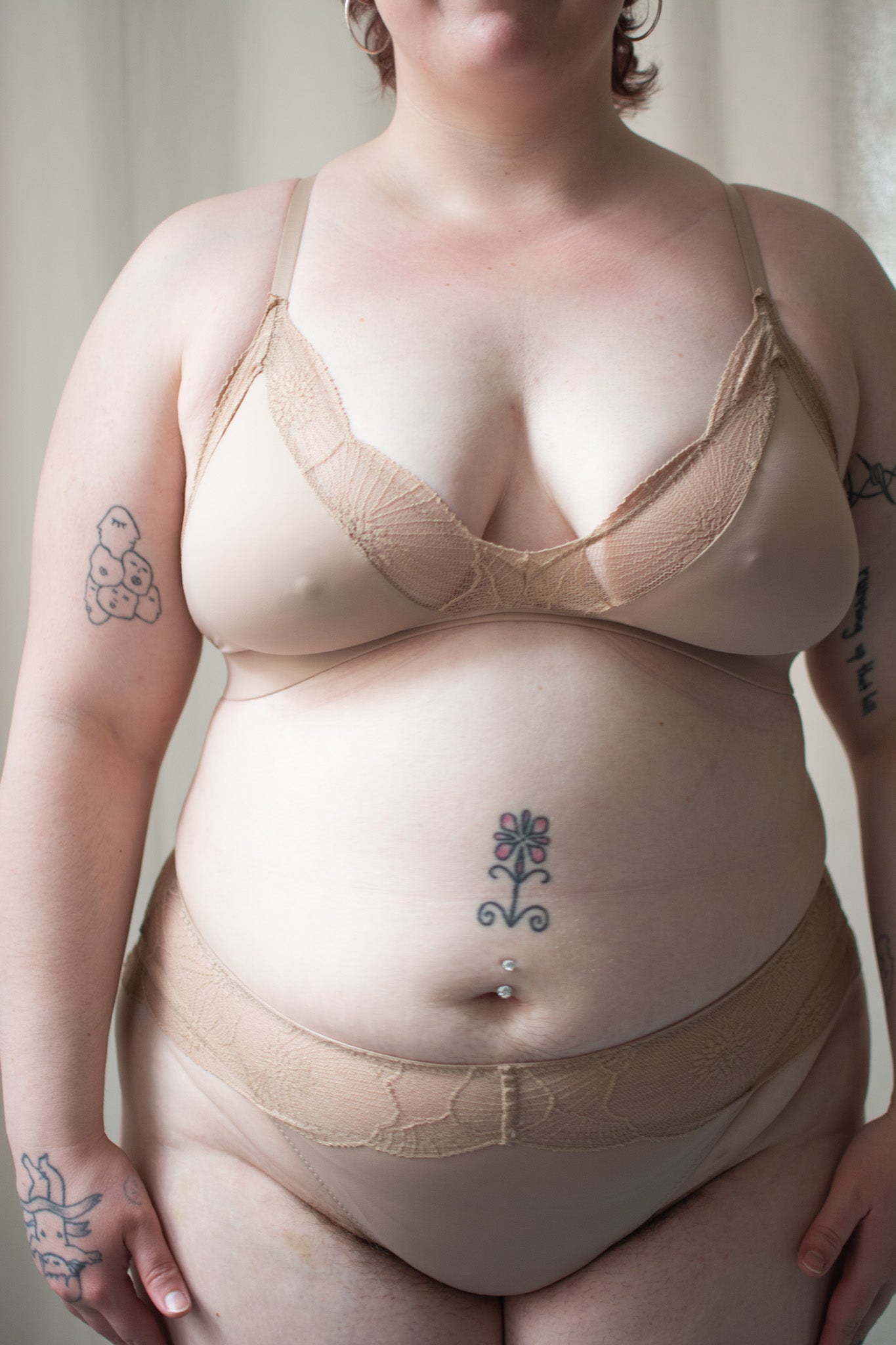 Person wearing beige lace bra and underwear against a neutral background.