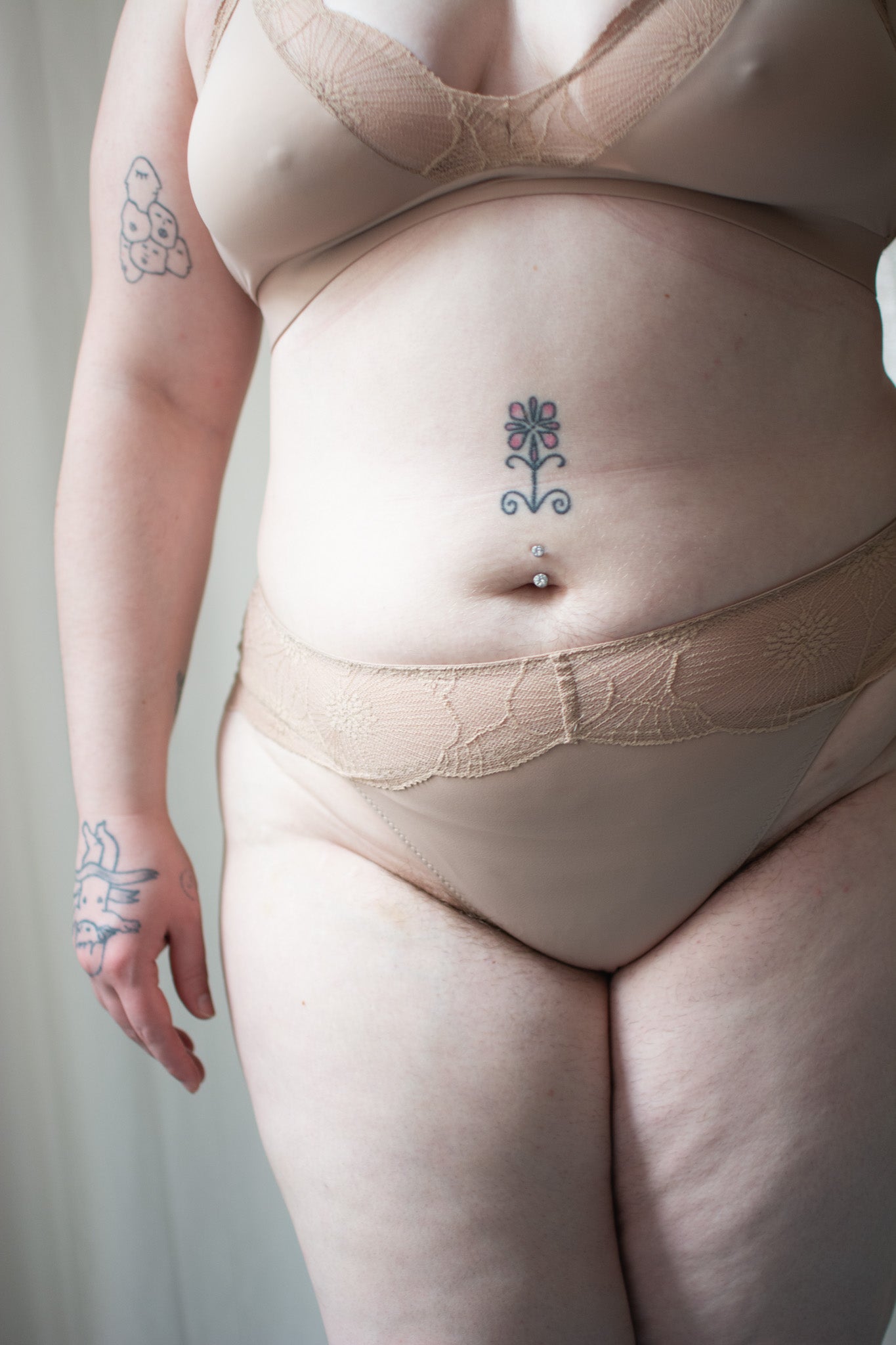 Person wearing beige lace bra and underwear against a neutral background.