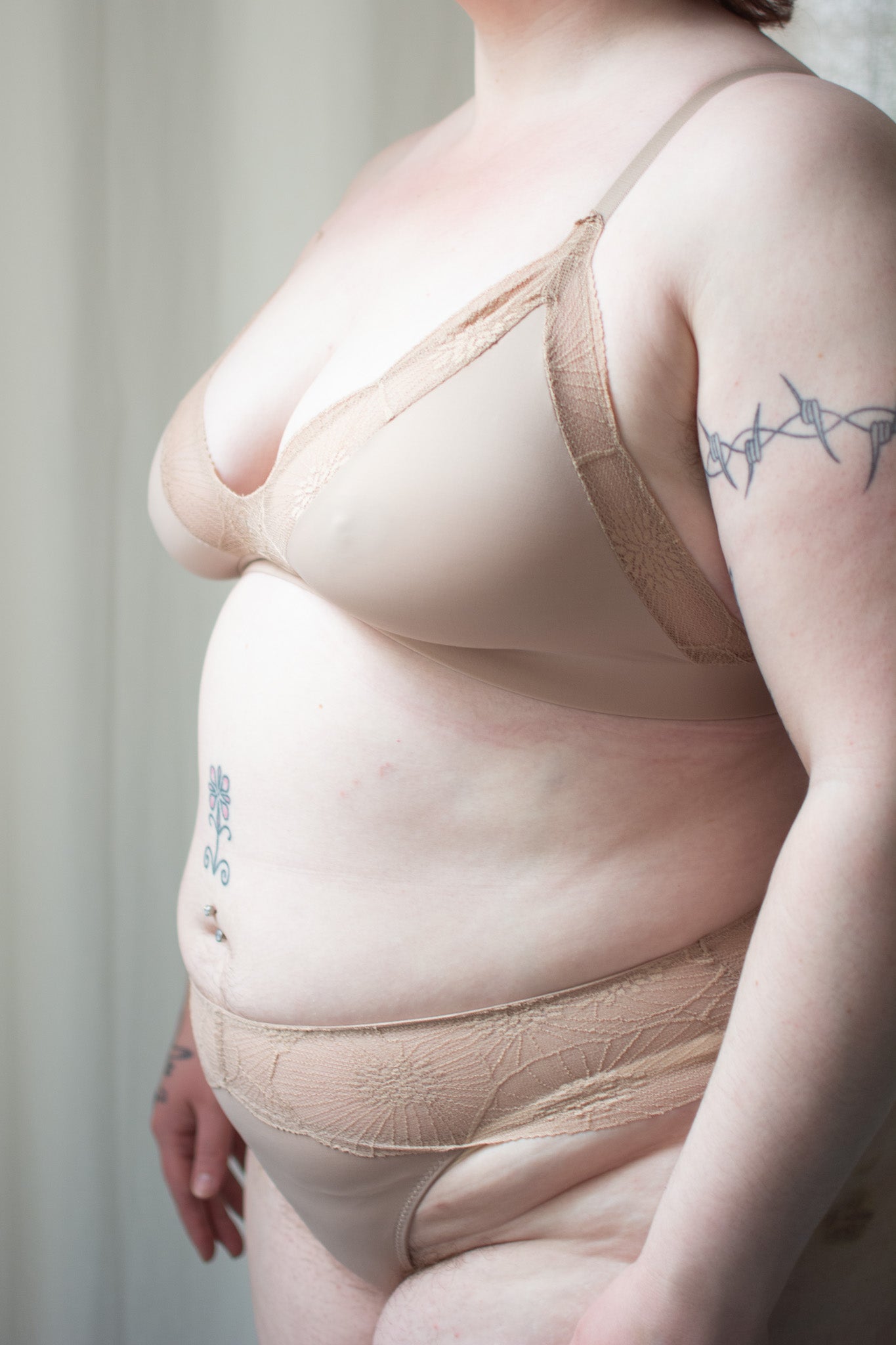 Person wearing beige lace bra and underwear against a neutral background.