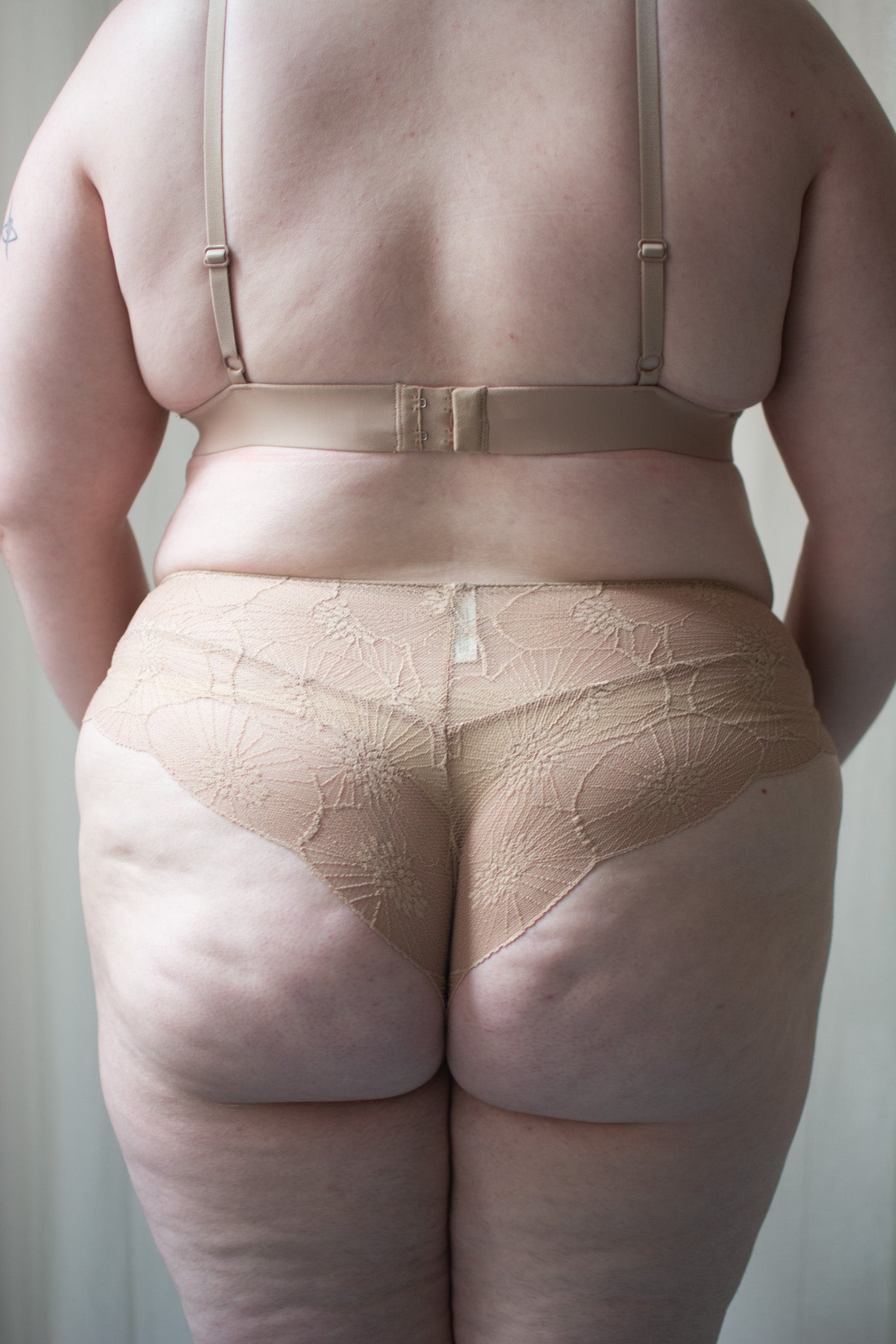 Person wearing beige lace bra and underwear against a neutral background.