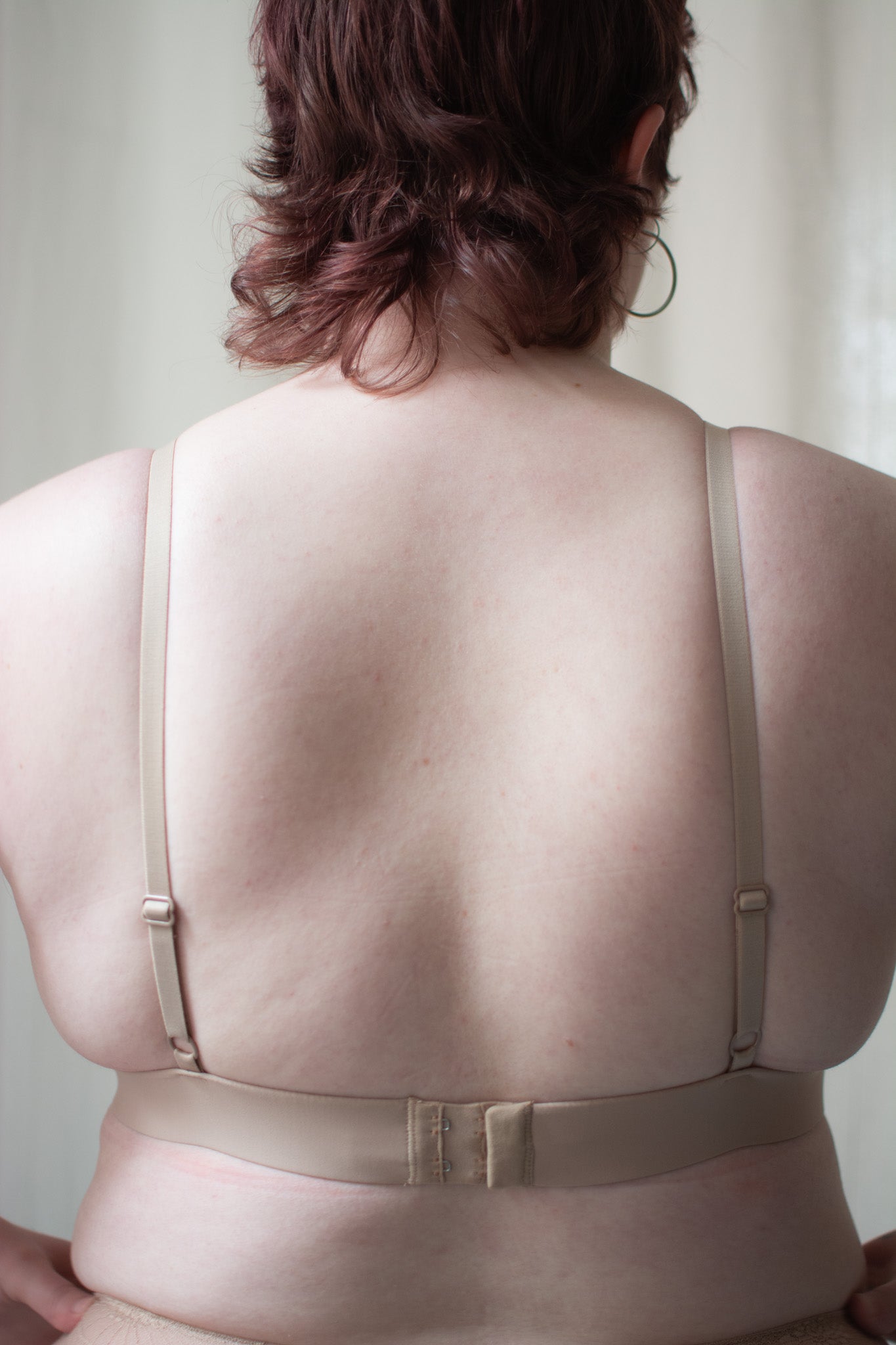 Beige lace bralette on a person with a neutral background.
