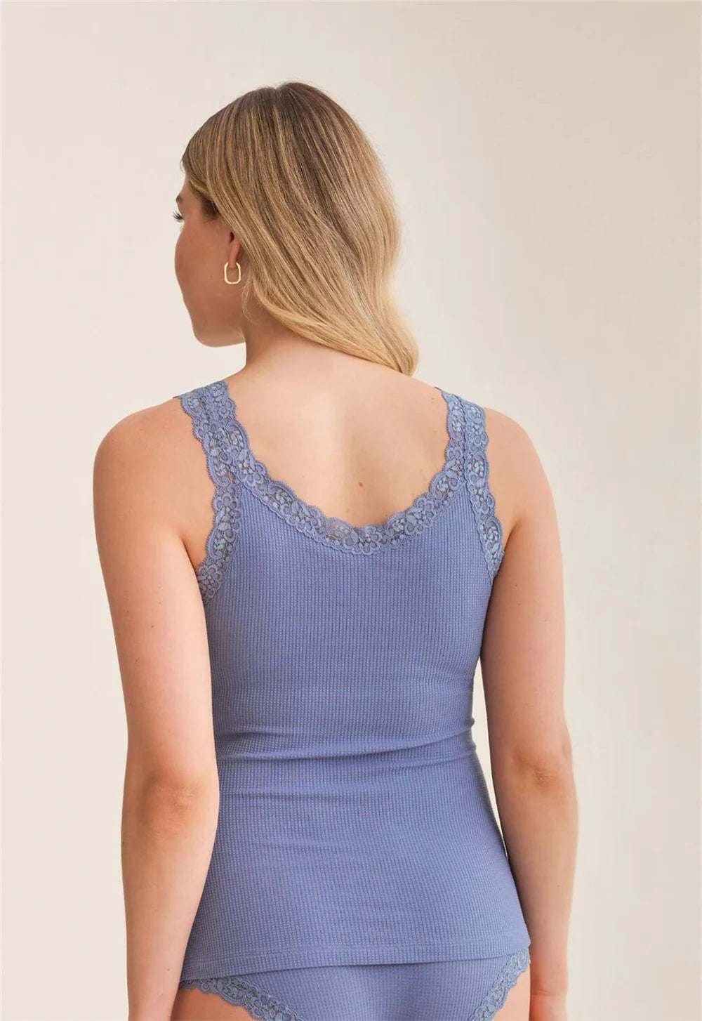 Woman wearing a blue ribbed tank top with lace details on a beige background