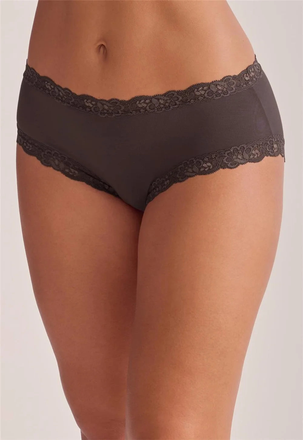 A close-up of a model wearing dark brown lace-trimmed briefs against a plain light gray studio background.