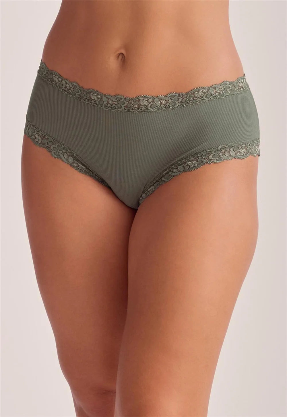 A close-up of a model wearing thyme green ribbed underwear with matching lace trim at the waistband and leg openings, set against a plain light beige studio background.
