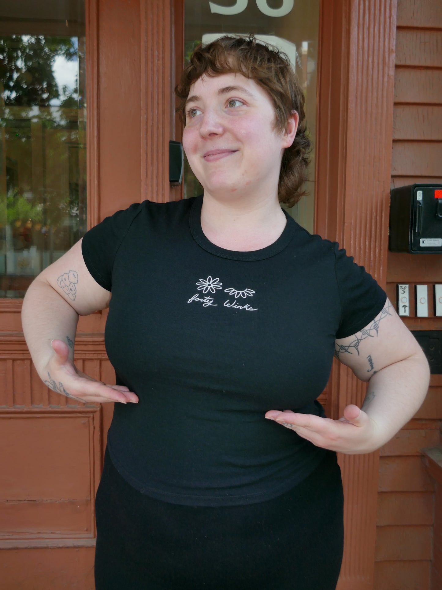 Person wearing a black t-shirt with a logo in front of a building entrance