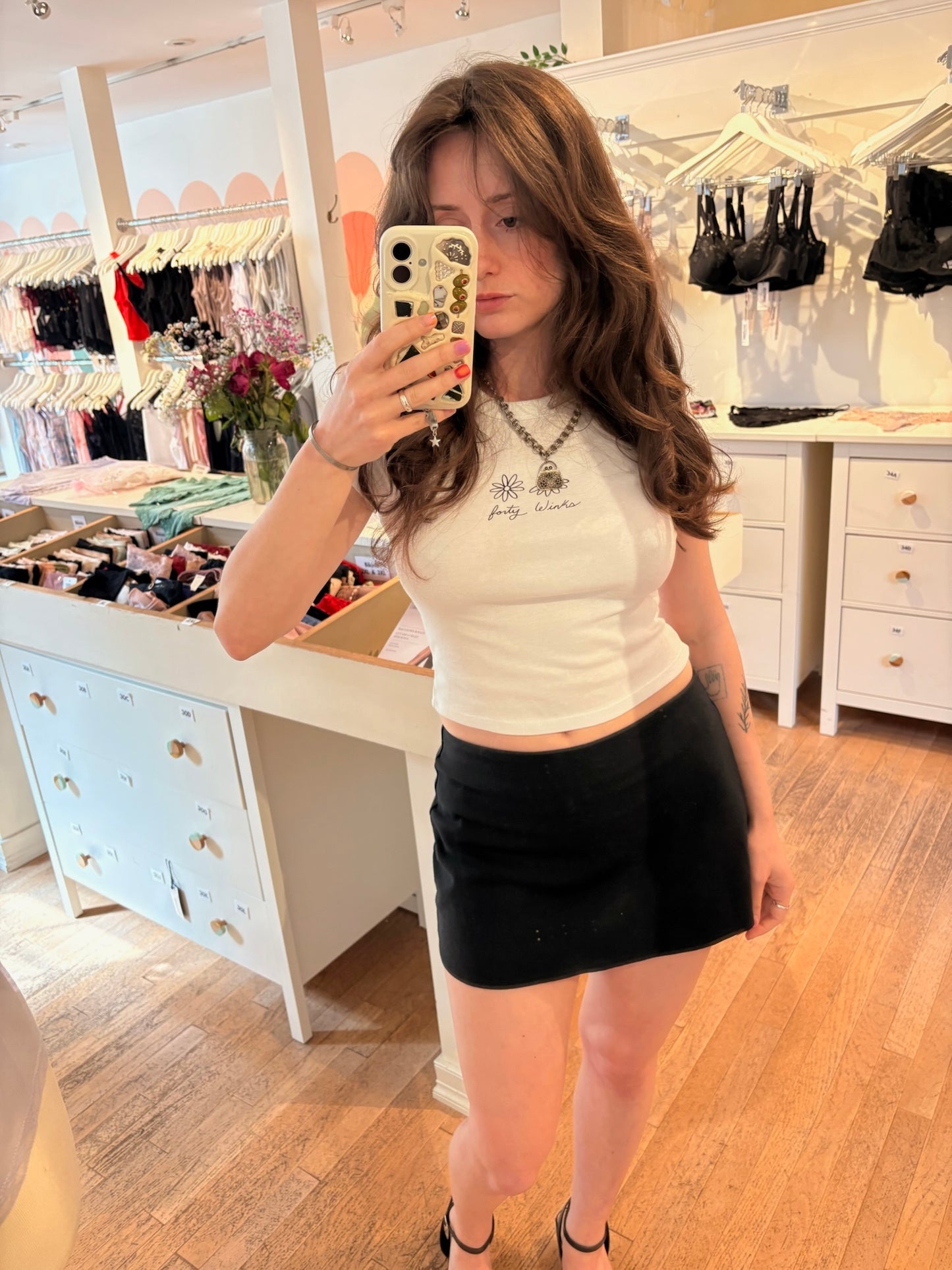 Woman taking a mirror selfie in a store wearing a white crop top and black skirt.