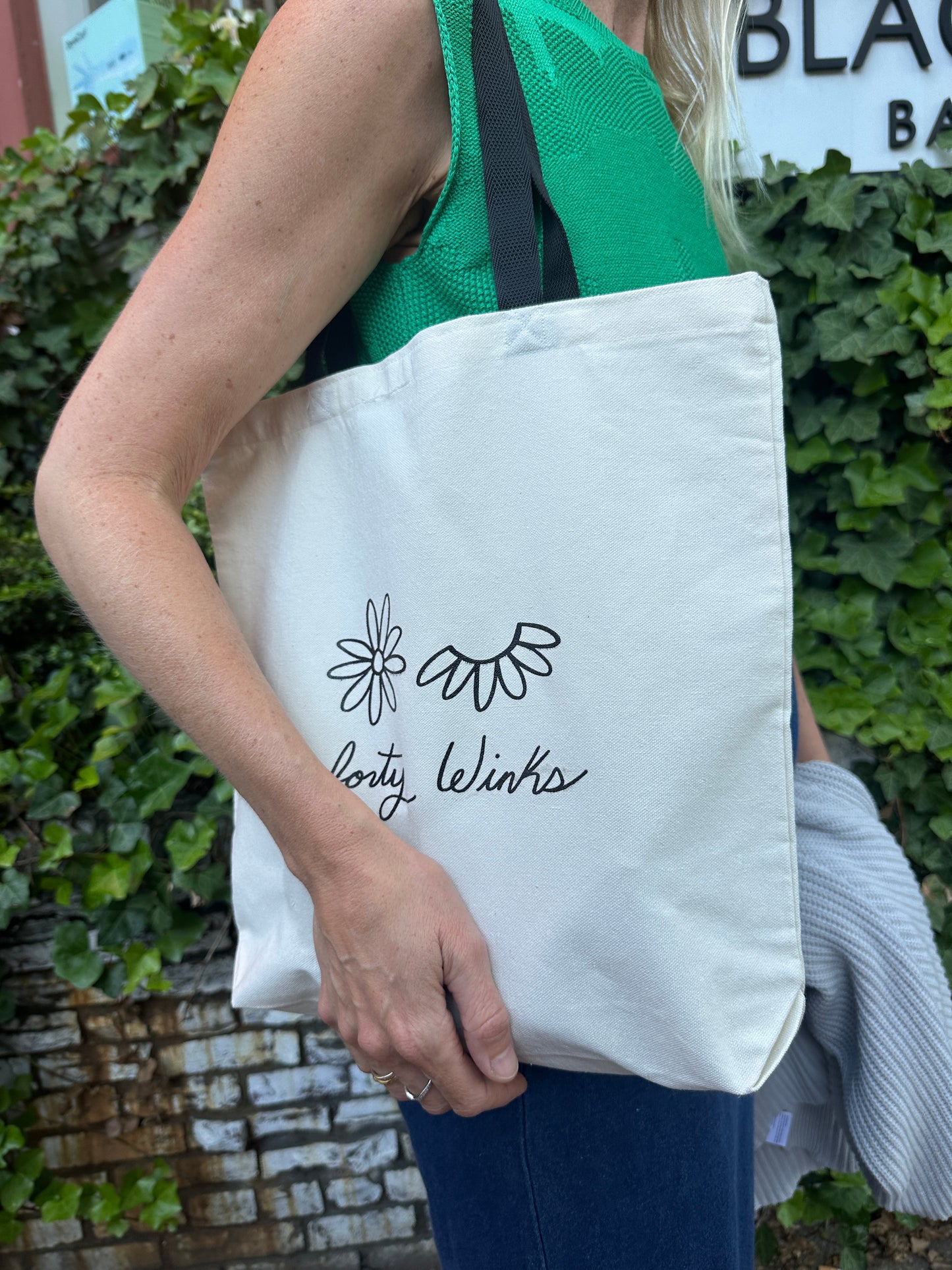 Person holding a white tote bag with floral design and text.