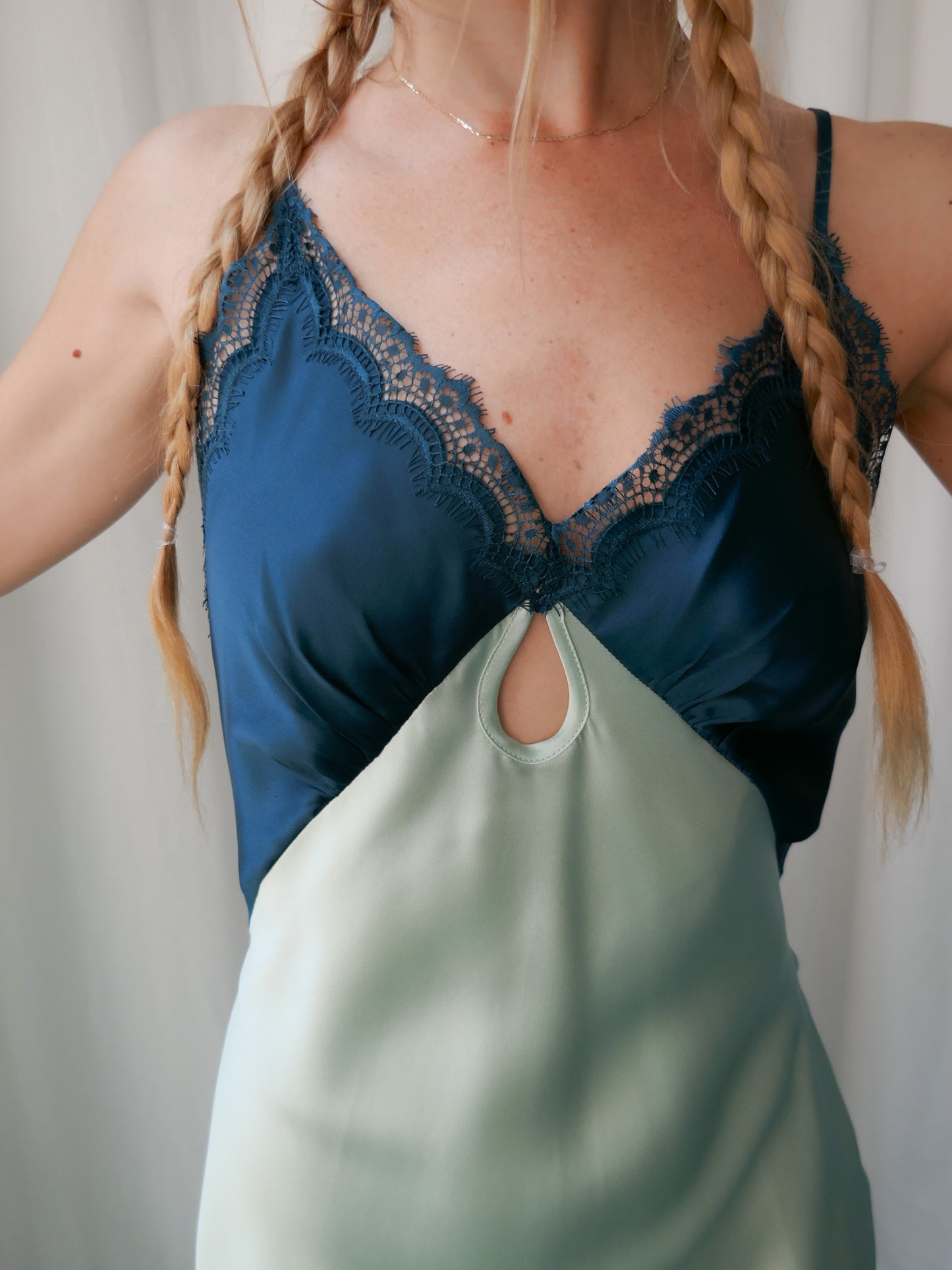 Woman wearing a blue lace-trimmed top with a green bag over her shoulder against a neutral background