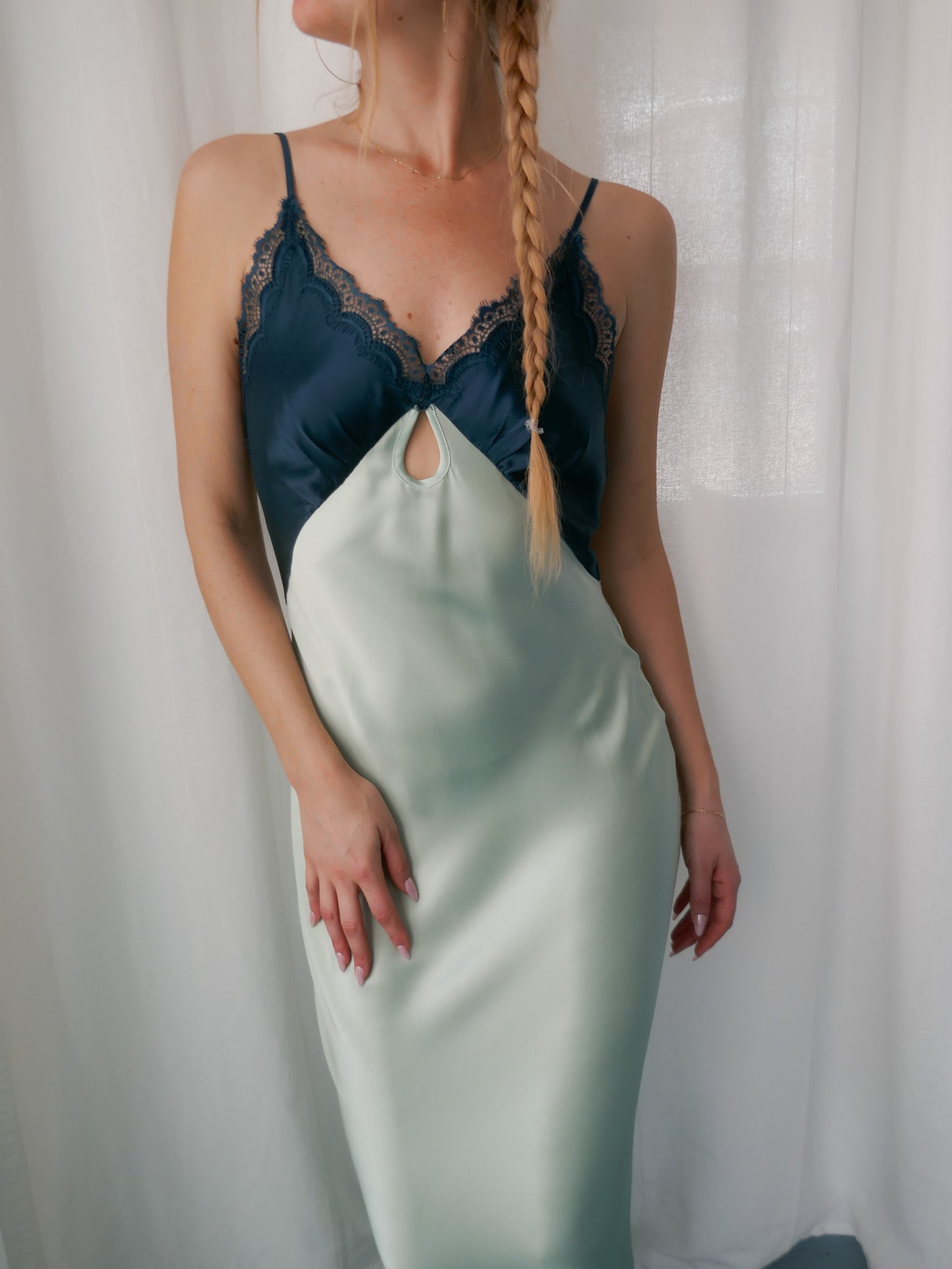 Woman wearing a two-tone dress with a blue top and light green skirt against a white curtain background.