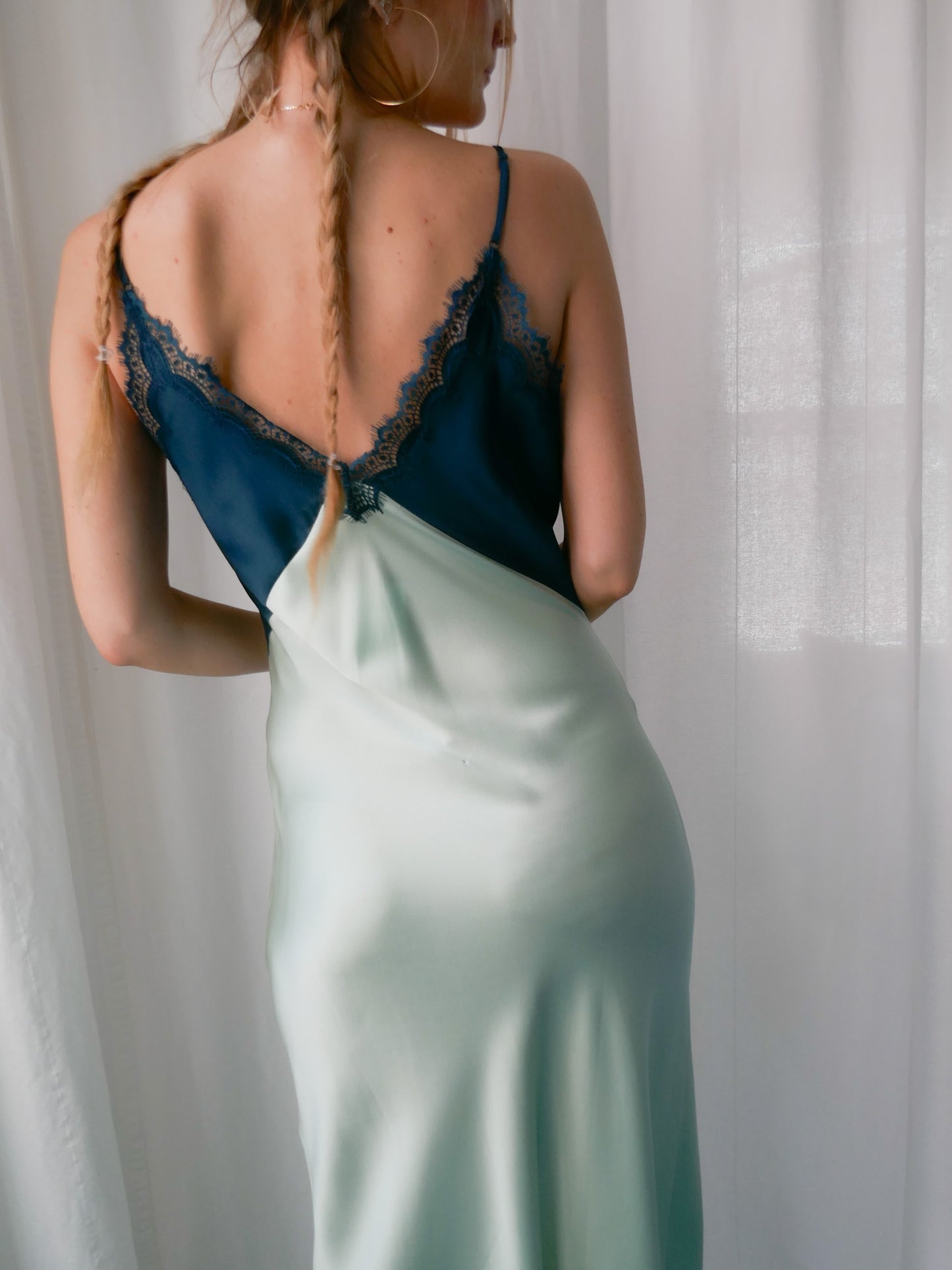 Woman wearing a two-tone dress with a backless design, standing against a white curtain.