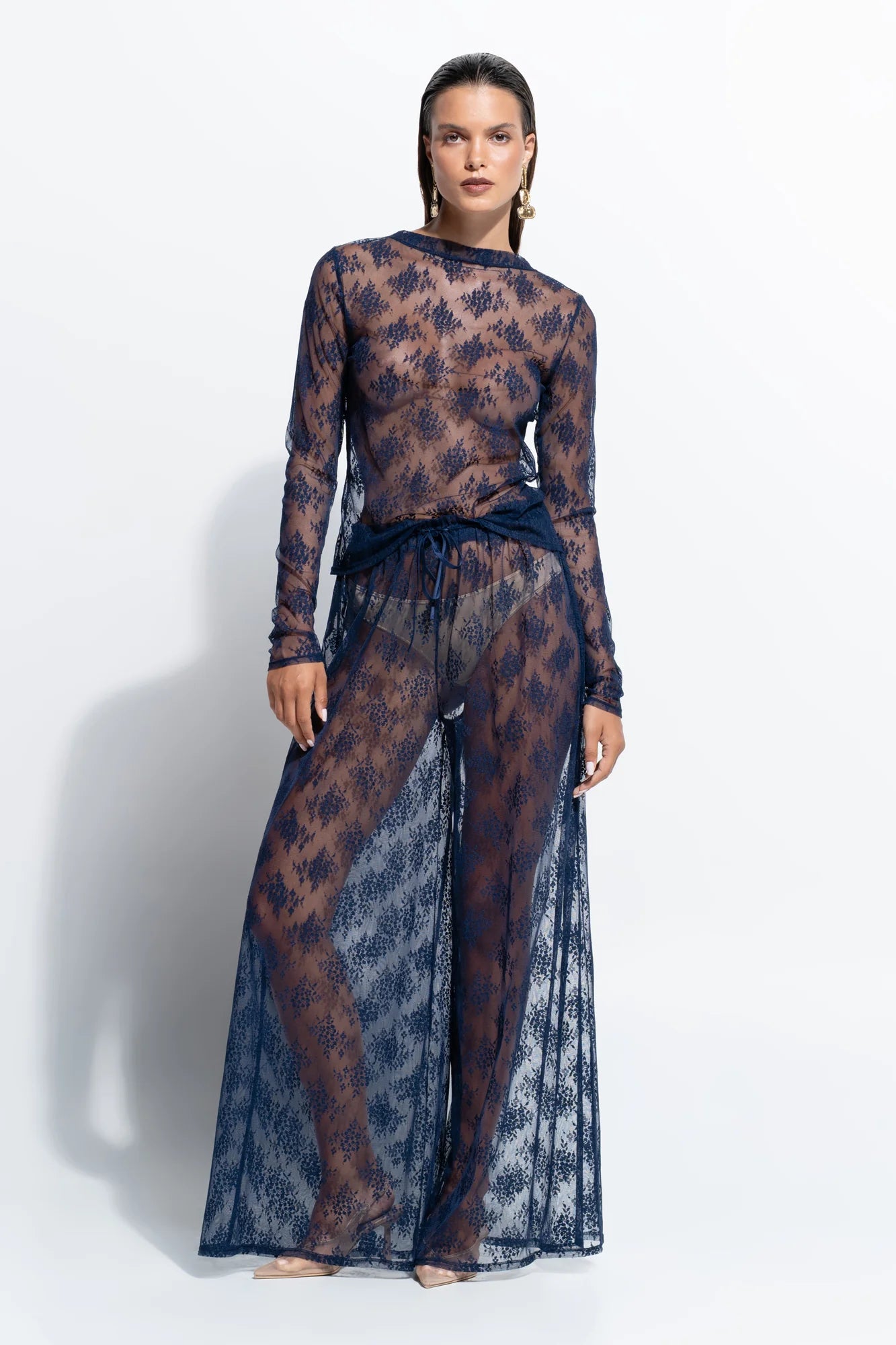 person wearing blue sheer lace shirt and pants against a white background.