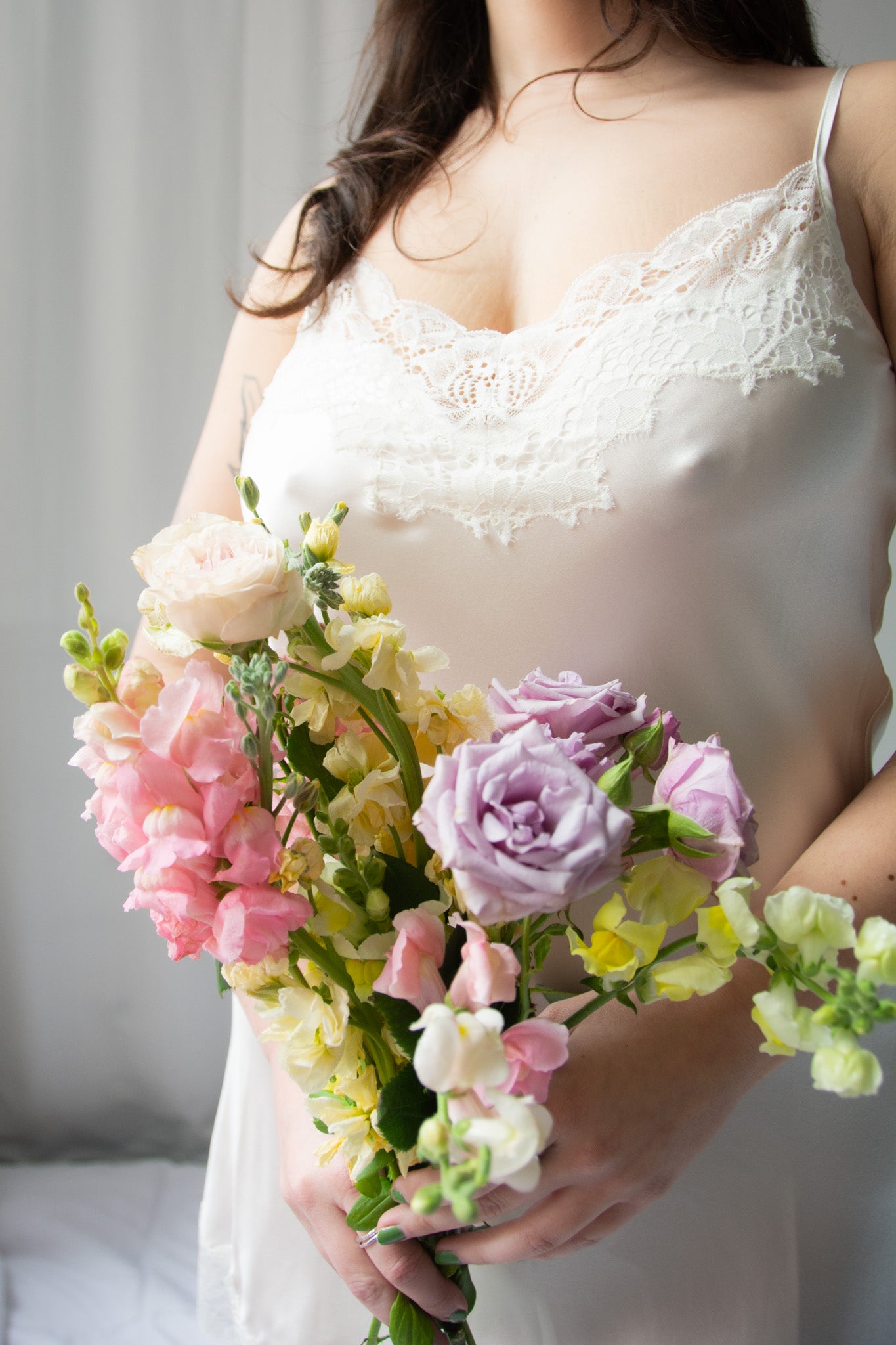 person wearing white silk chemise with lace holding a bouquet of flowers against a white background