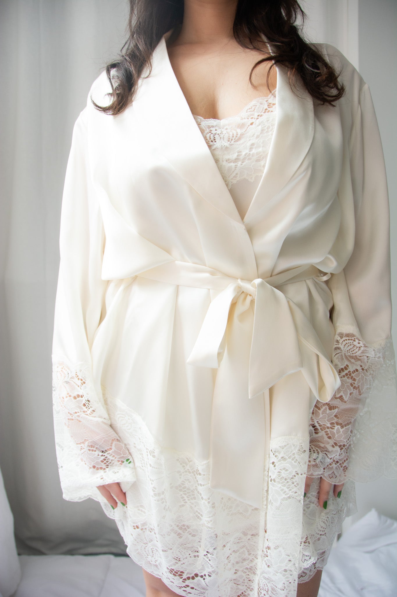 A woman wearing a beige silk lace robe with a shawl collar and 3/4 length sleeves, tied with a silk belt.
