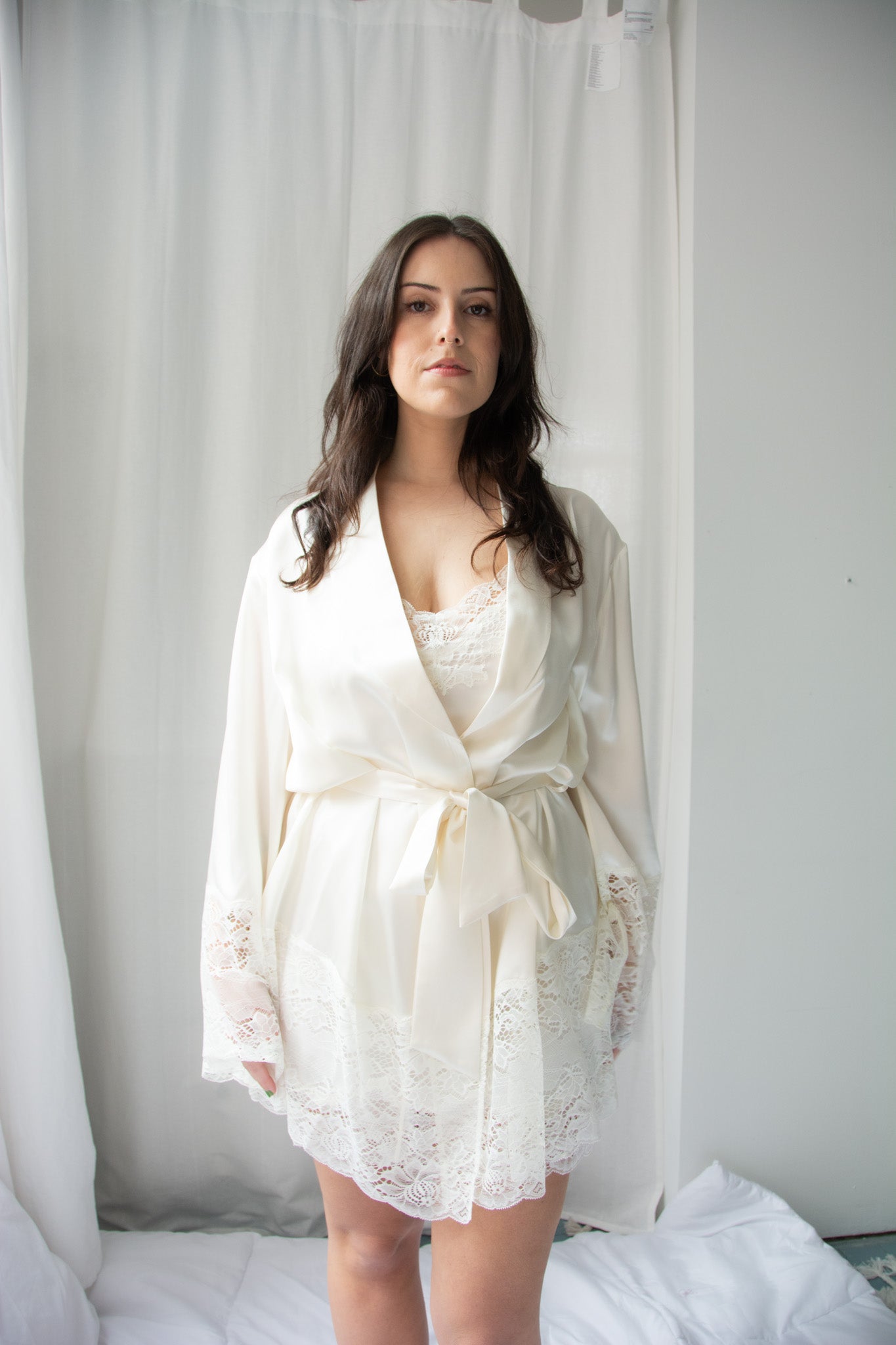 A woman wearing a beige silk lace robe with a shawl collar and 3/4 length sleeves, tied with a silk belt.