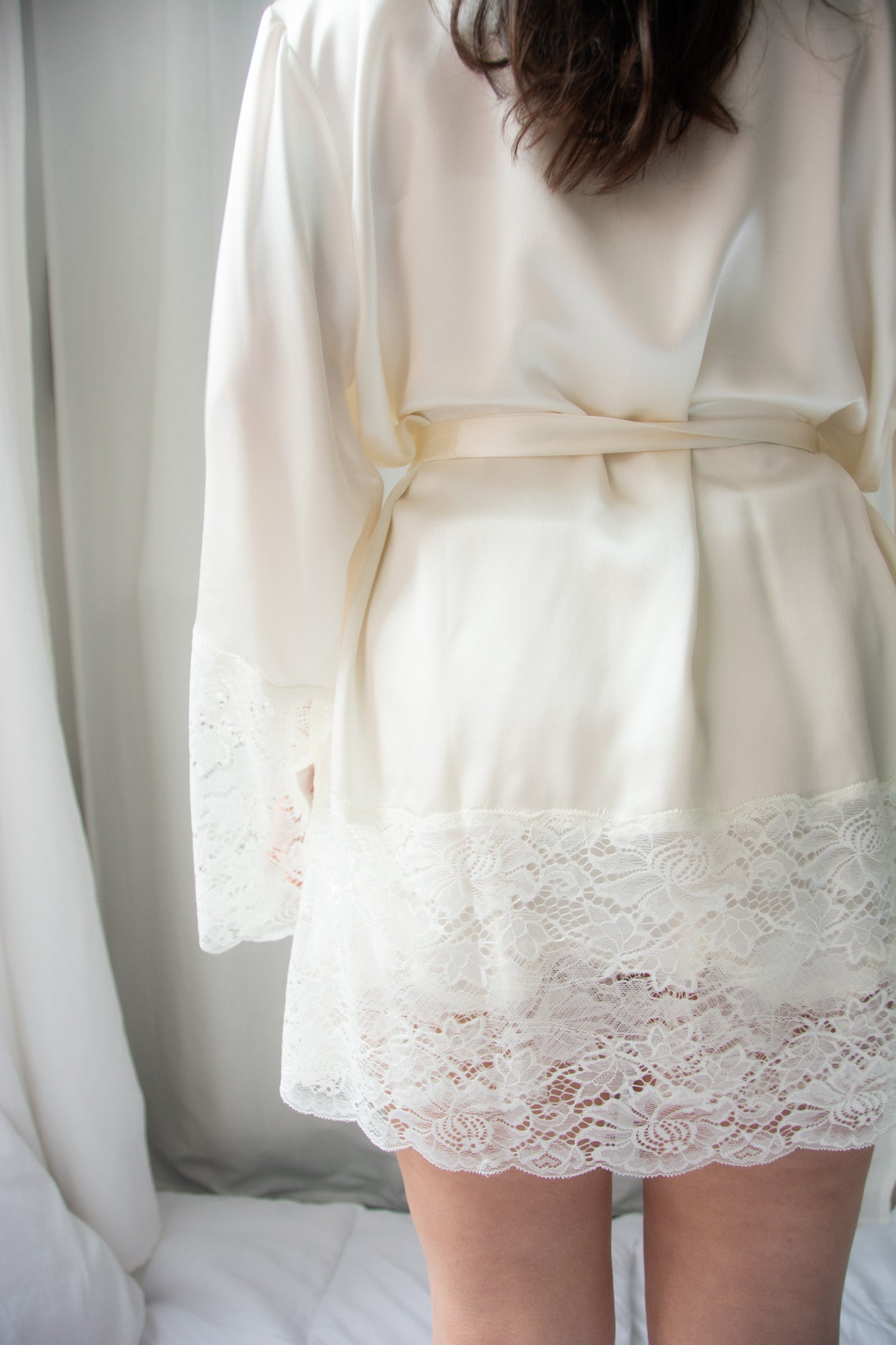 A woman wearing a beige silk lace robe with a shawl collar and 3/4 length sleeves, tied with a silk belt.