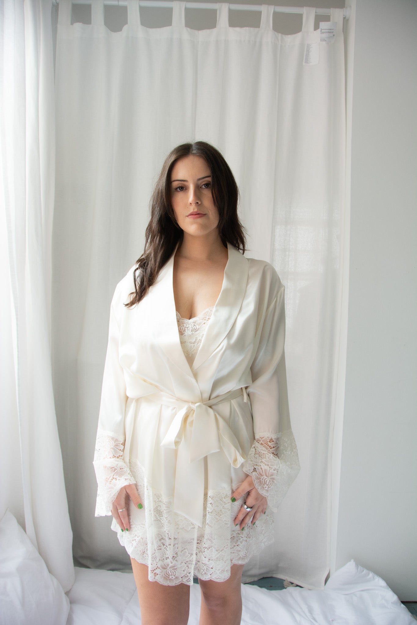 A woman wearing a beige silk lace robe with a shawl collar and 3/4 length sleeves, tied with a silk belt.