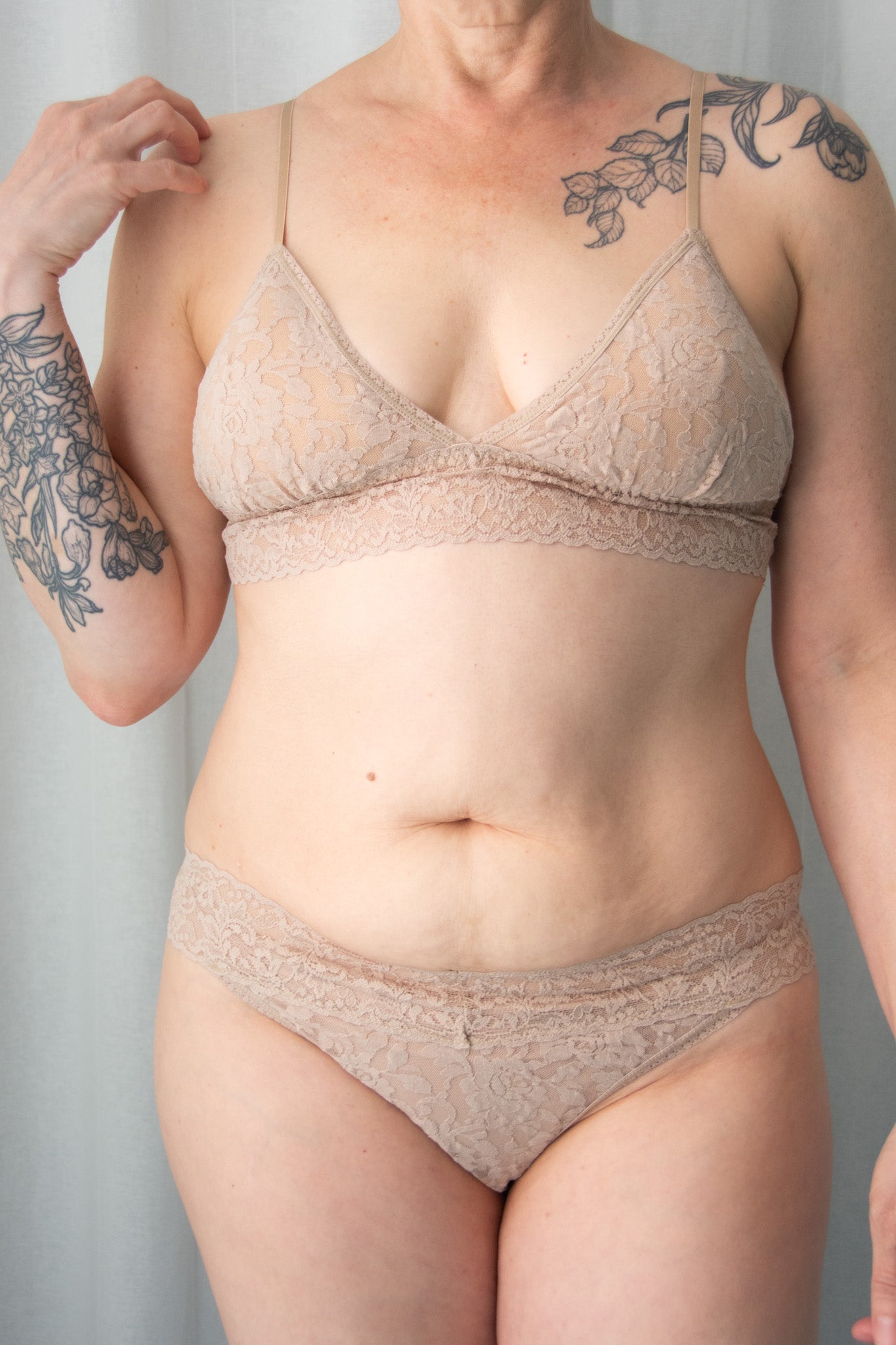 Person wearing a beige lace bra and panties set against a plain background
