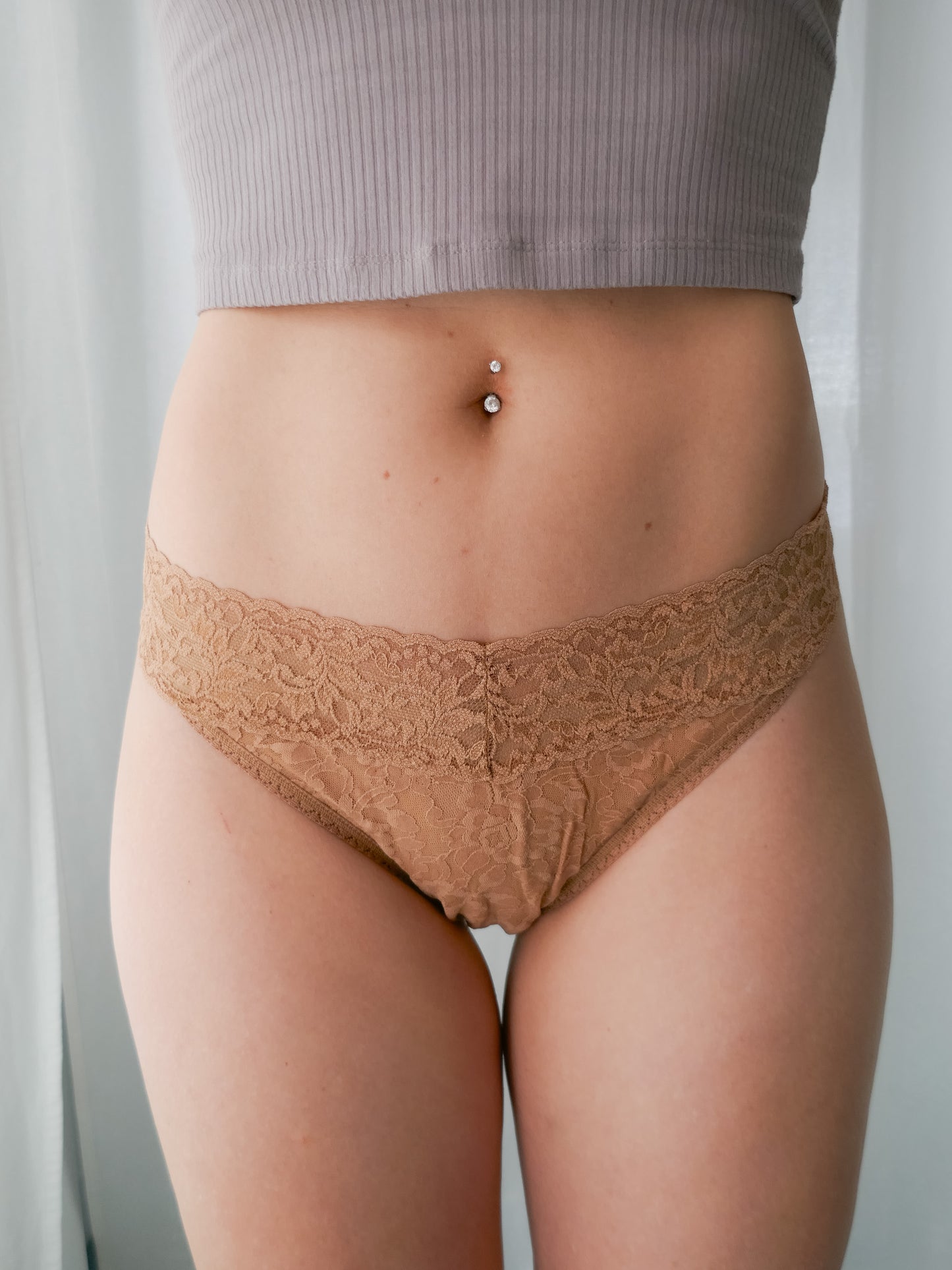 Person wearing beige lace underwear against a neutral background