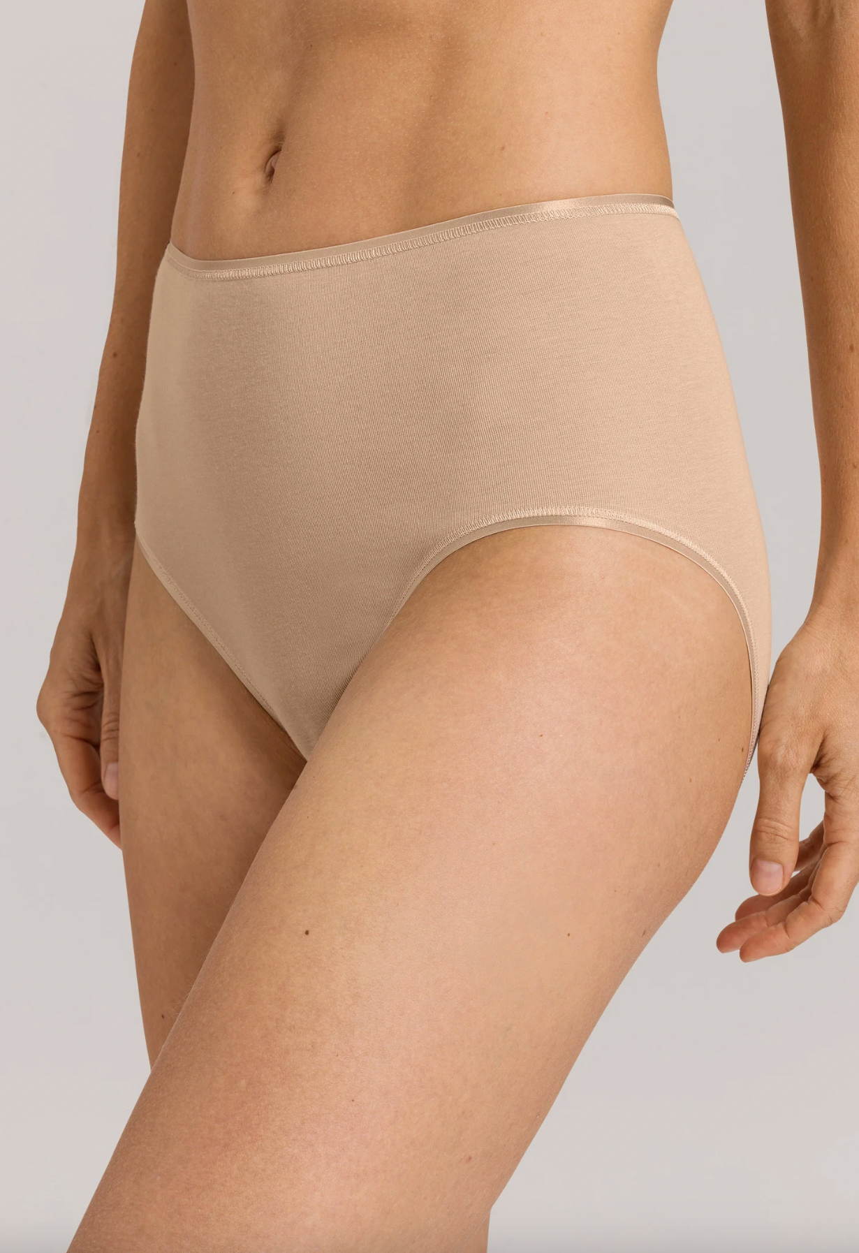 A close-up of a model wearing high-waisted, seamless underwear in a light beige shade against a neutral gray background.
