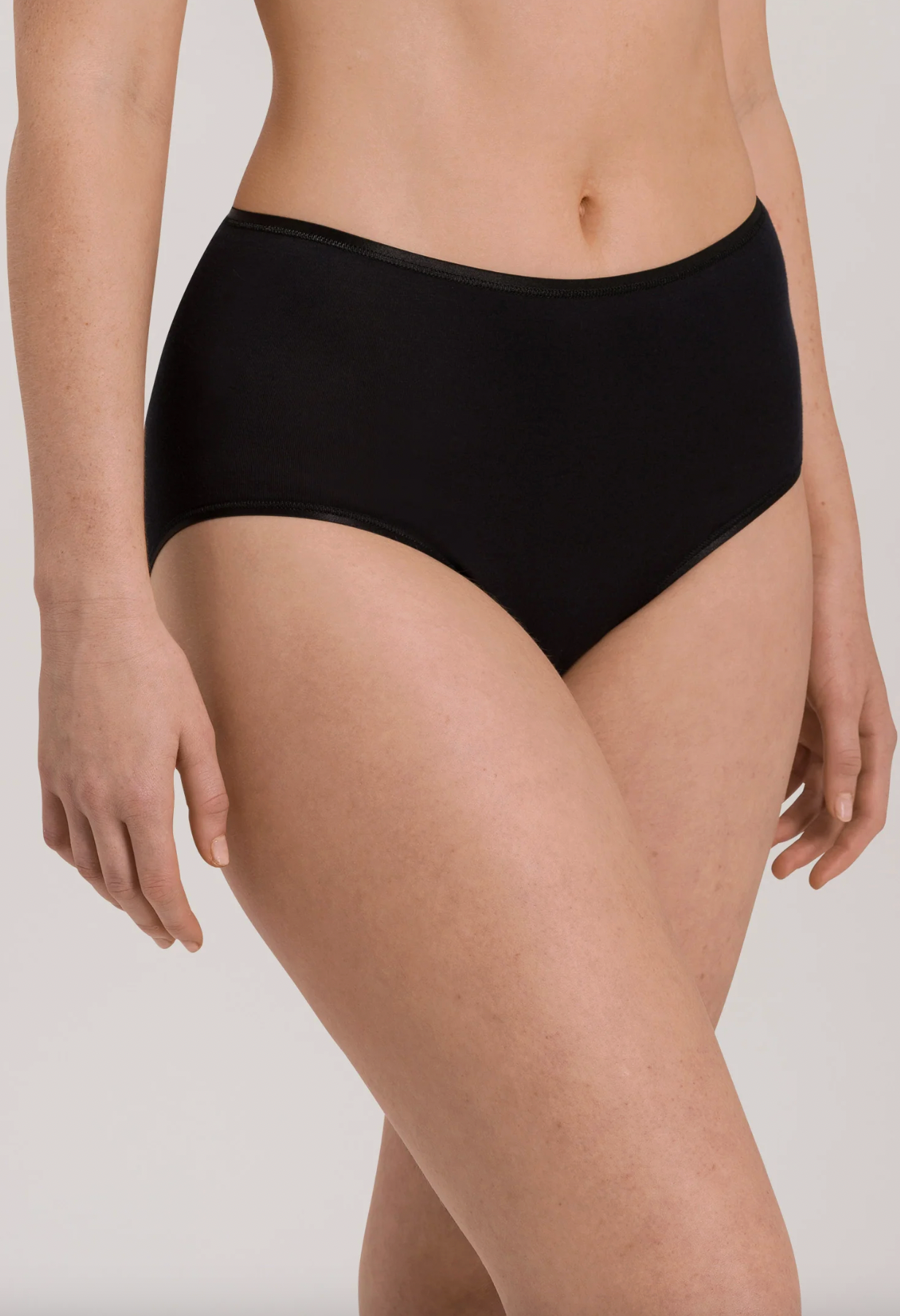 A close-up of a model wearing black high-waisted briefs against a light gray studio background.