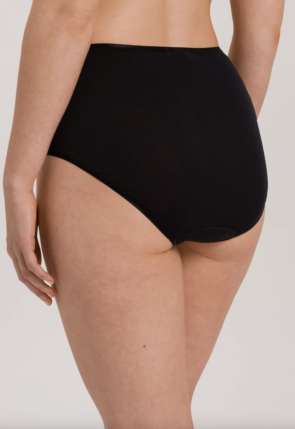 Rear view of a model wearing high-waisted black briefs against a plain light gray studio background.