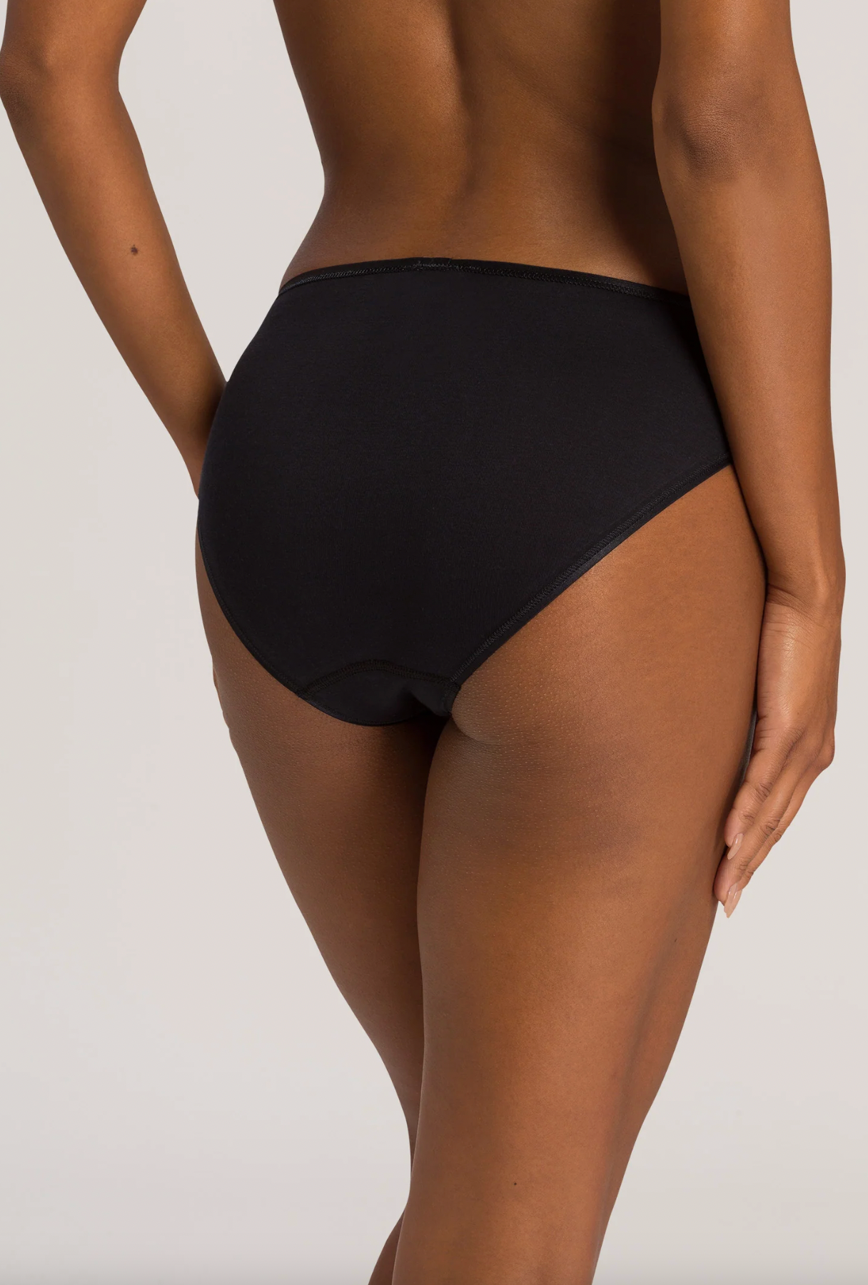 Rear view of a model wearing black high-waisted briefs against a light gray studio background.