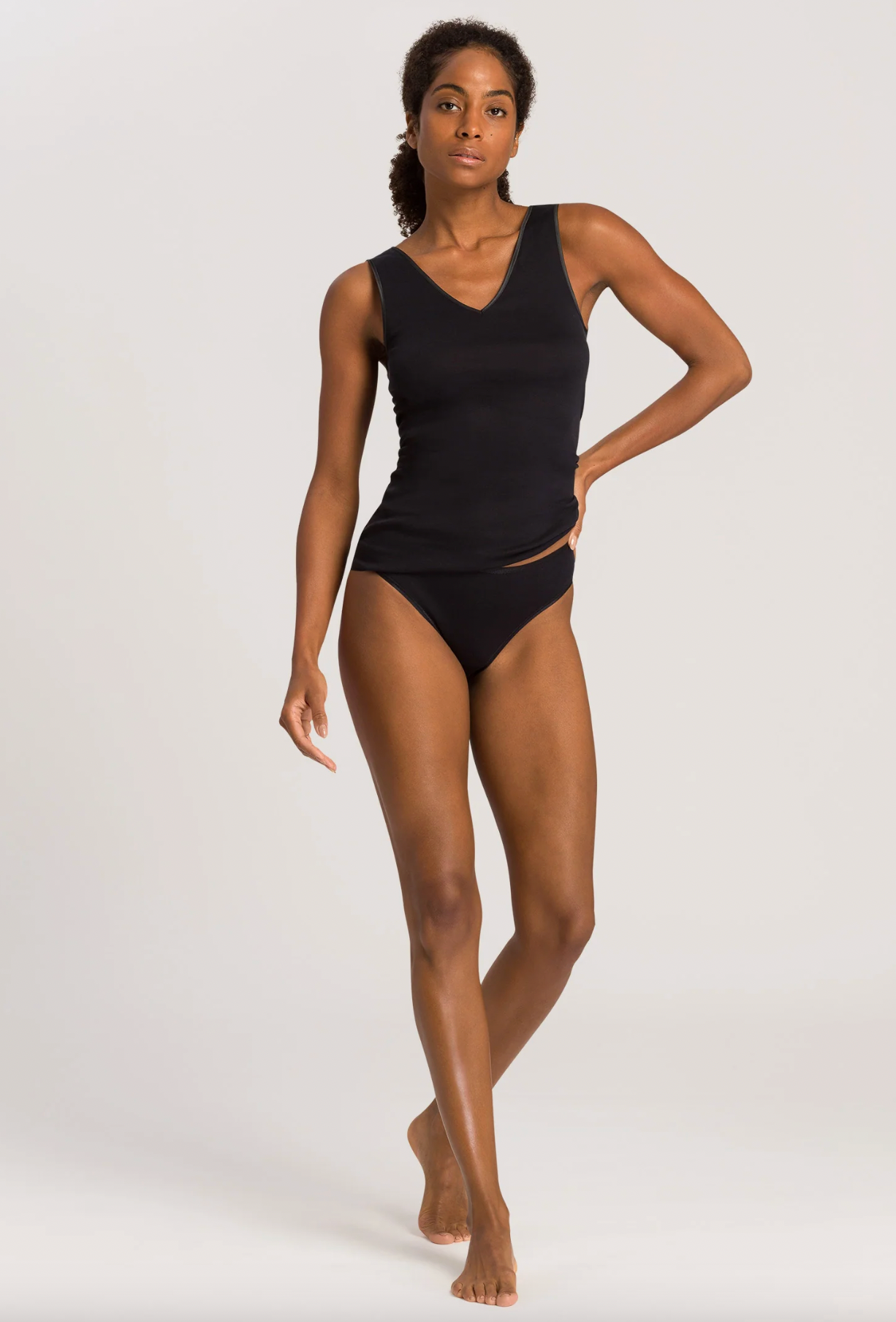 A woman modeling a black ribbed tank top and matching black high-waisted briefs against a light gray studio background.