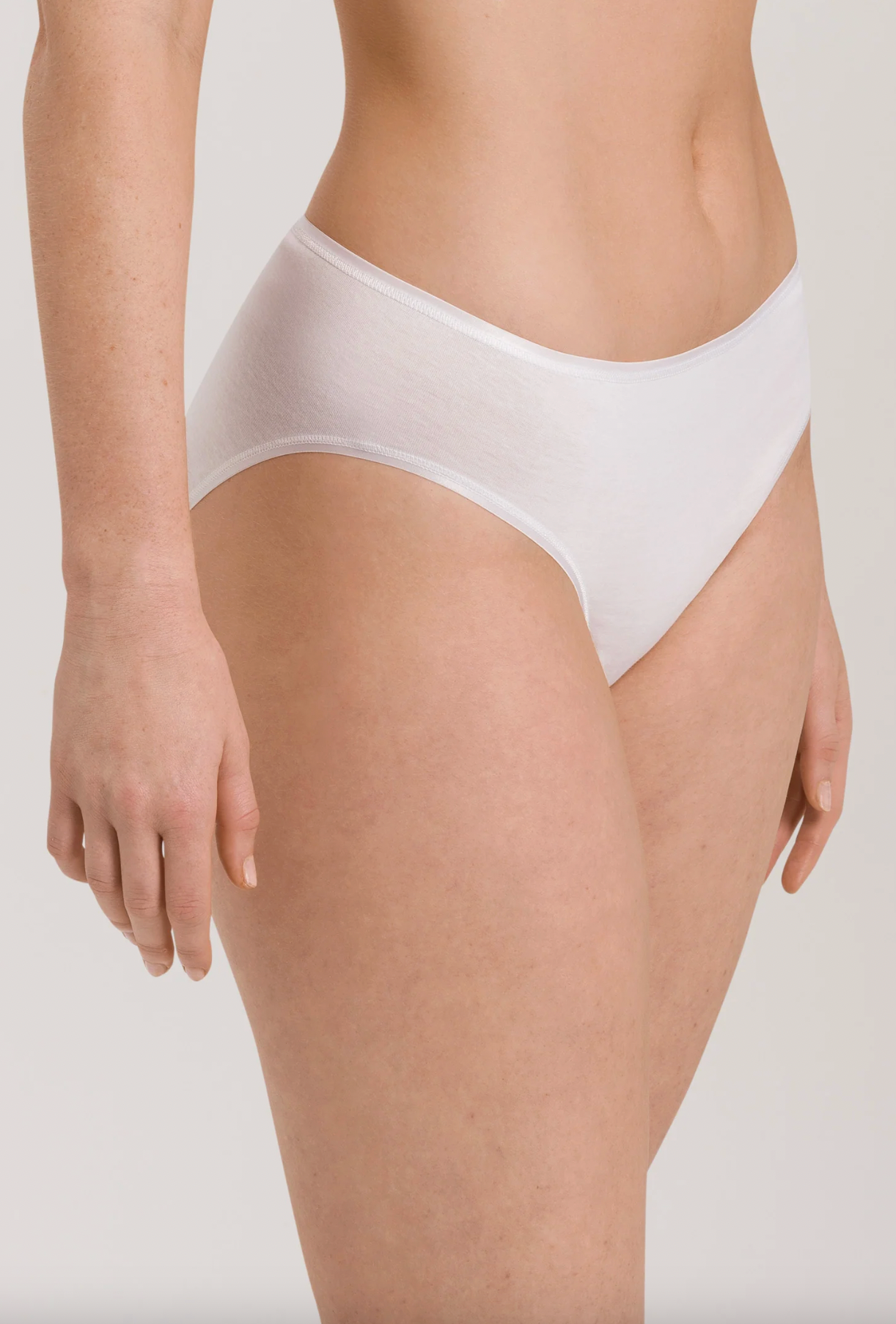 A close-up of a model wearing a pair of white high-waisted briefs against a light gray studio background.
